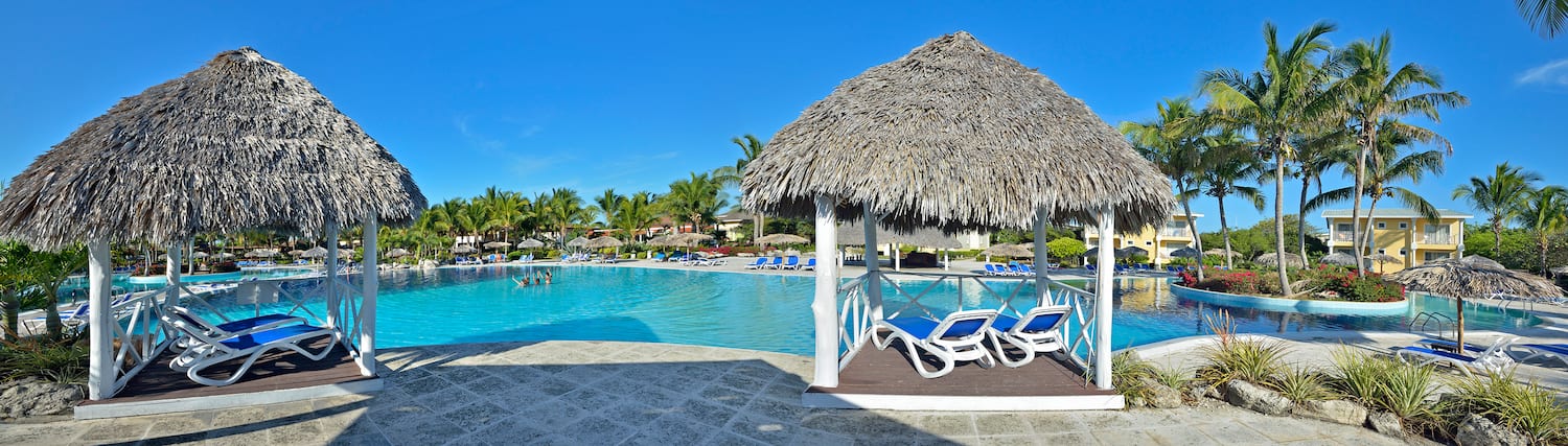 a pool with a thatched roof and lounge chairs