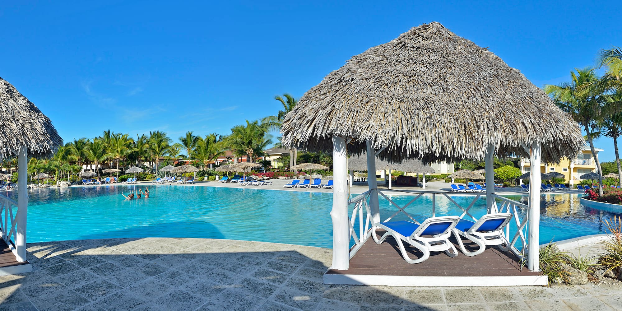 a pool with a thatched roof and lounge chairs