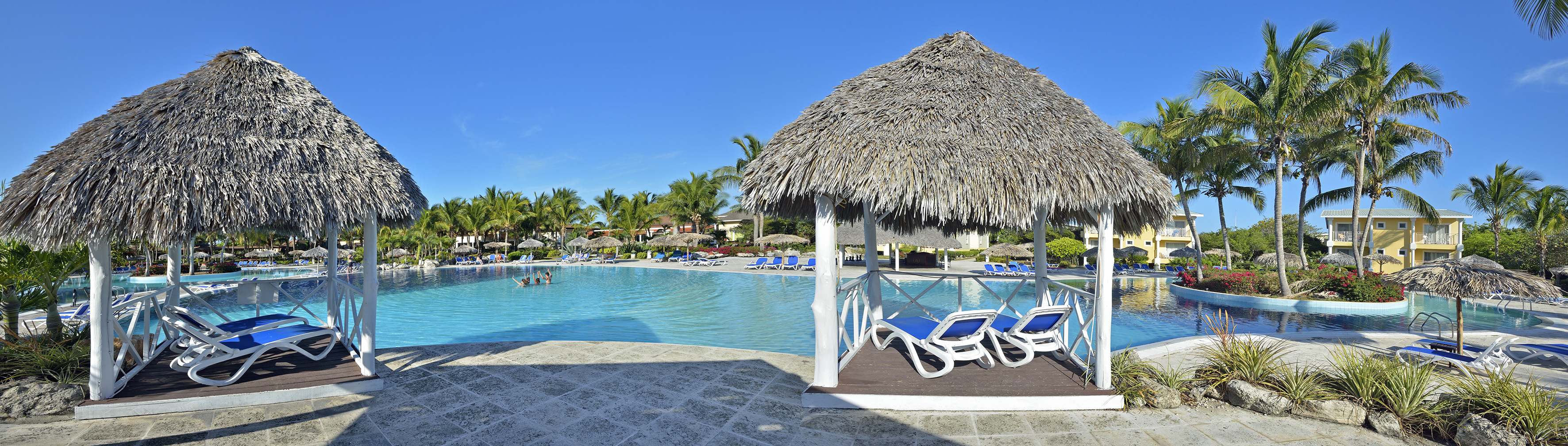 a pool with a thatched roof and lounge chairs