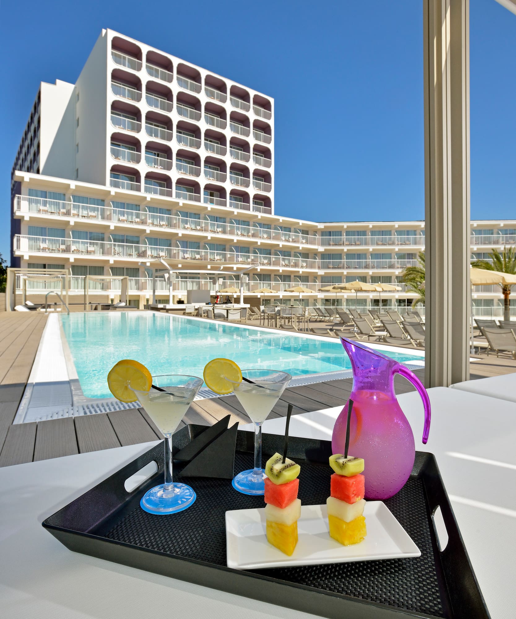 a tray of fruit and a pitcher on a table with a pool in the background