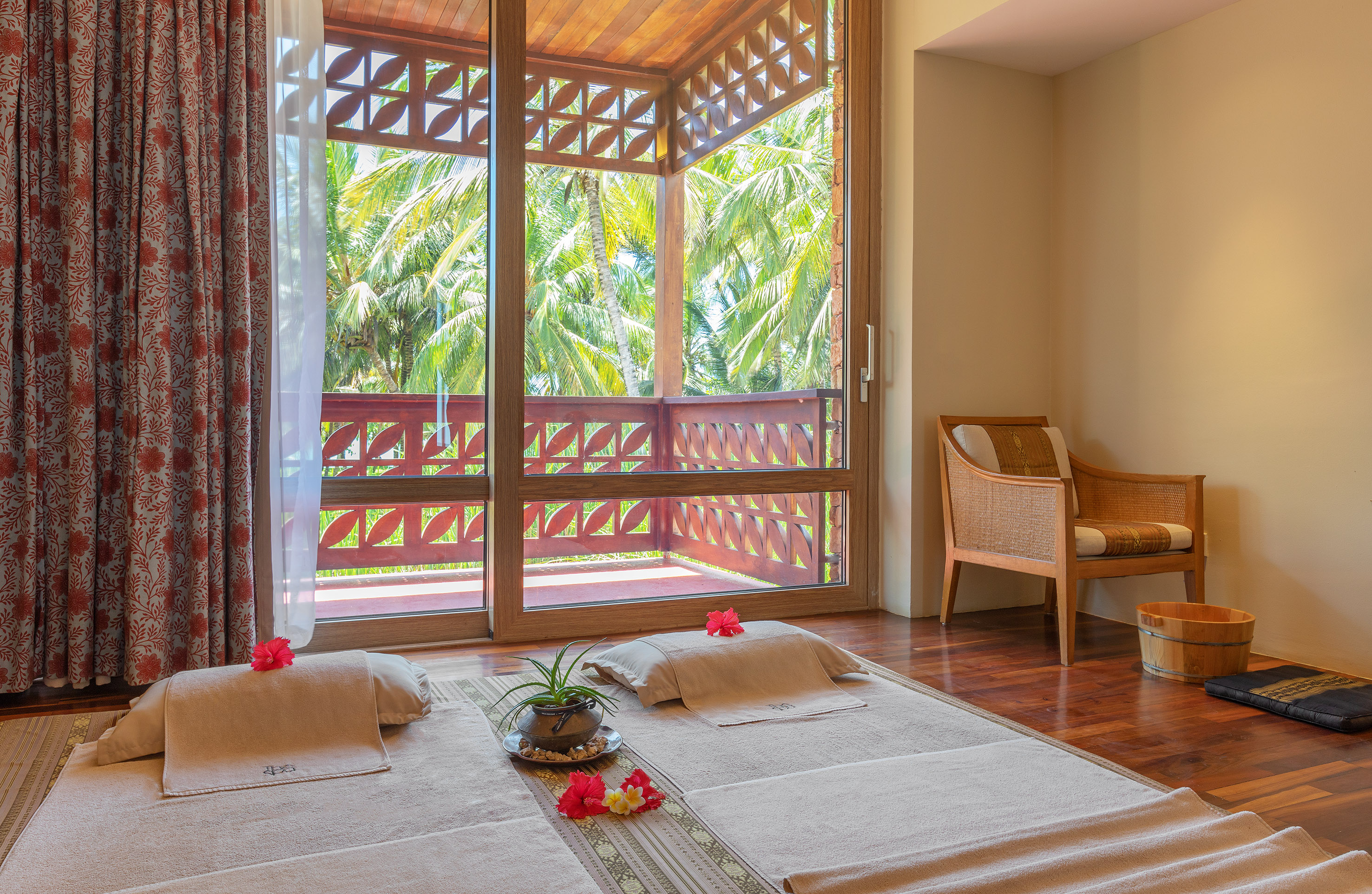 Tropical spa treatment room with floor beds, hibiscus, and balcony palm view.