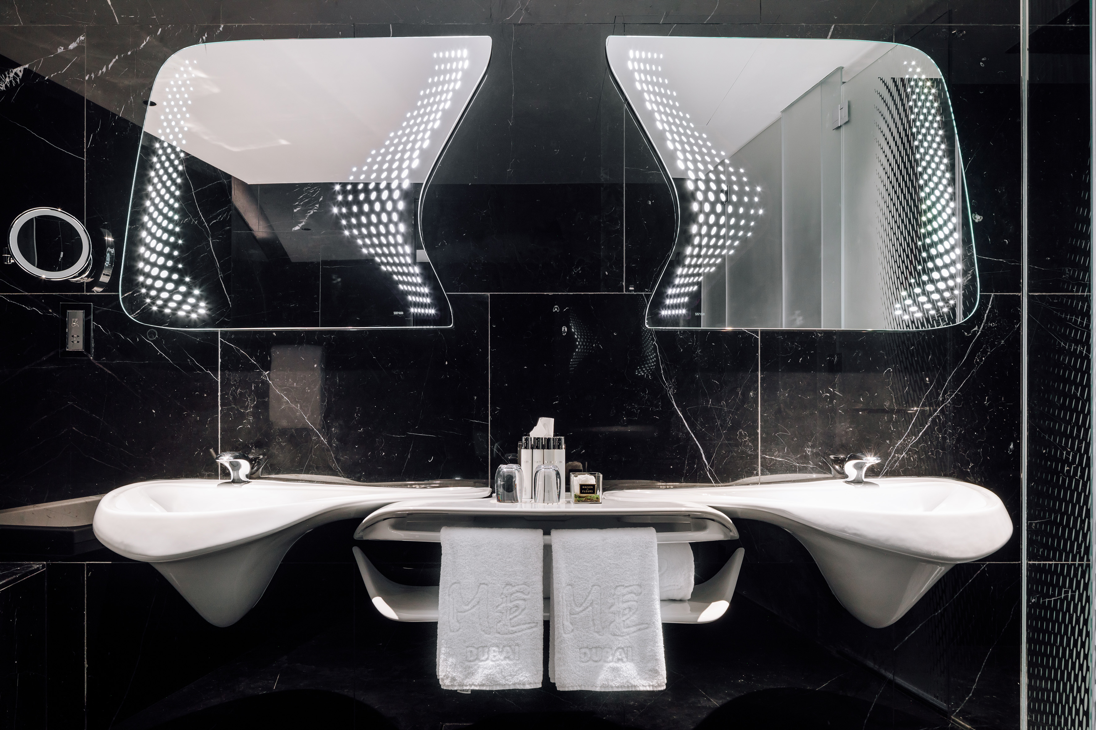 Modern hotel bathroom with dual sinks, LED mirrors, and black marble walls.