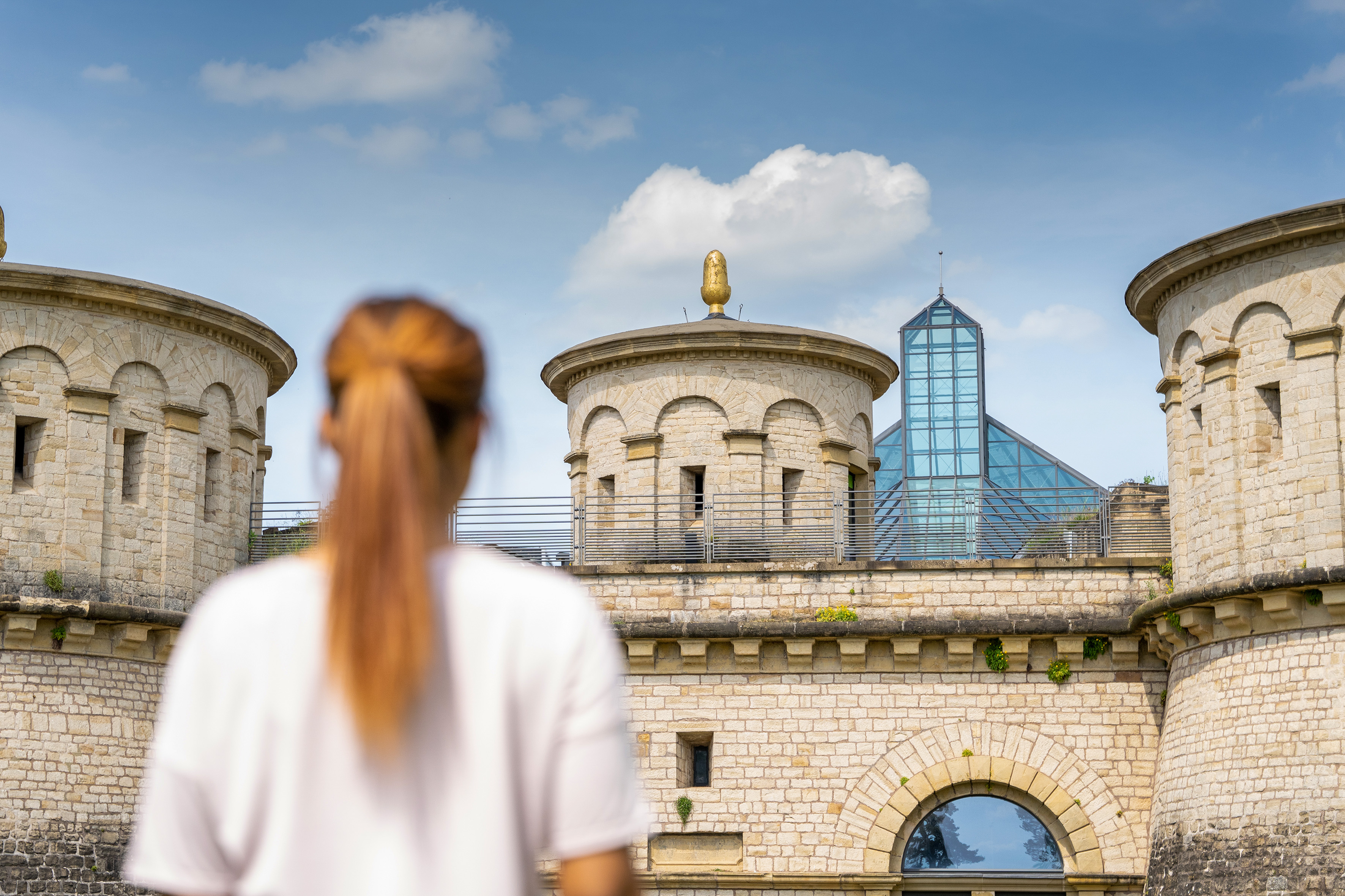 Stone fortress towers and modern glass building under a blue sky.