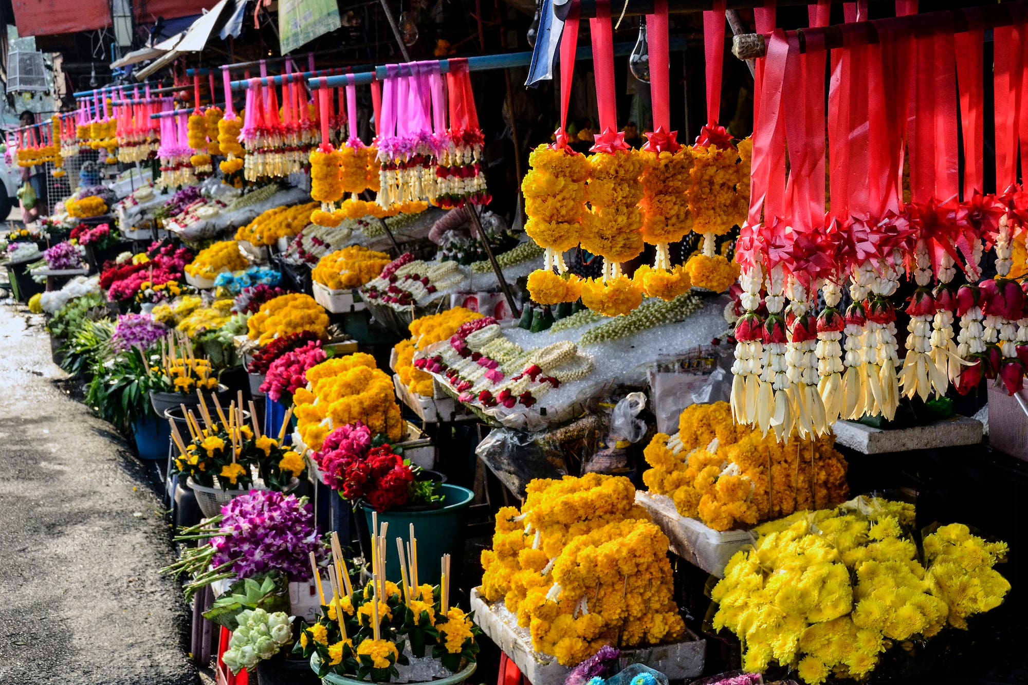 Colorful Thai flower market stall with hanging jasmine and marigold garlands.