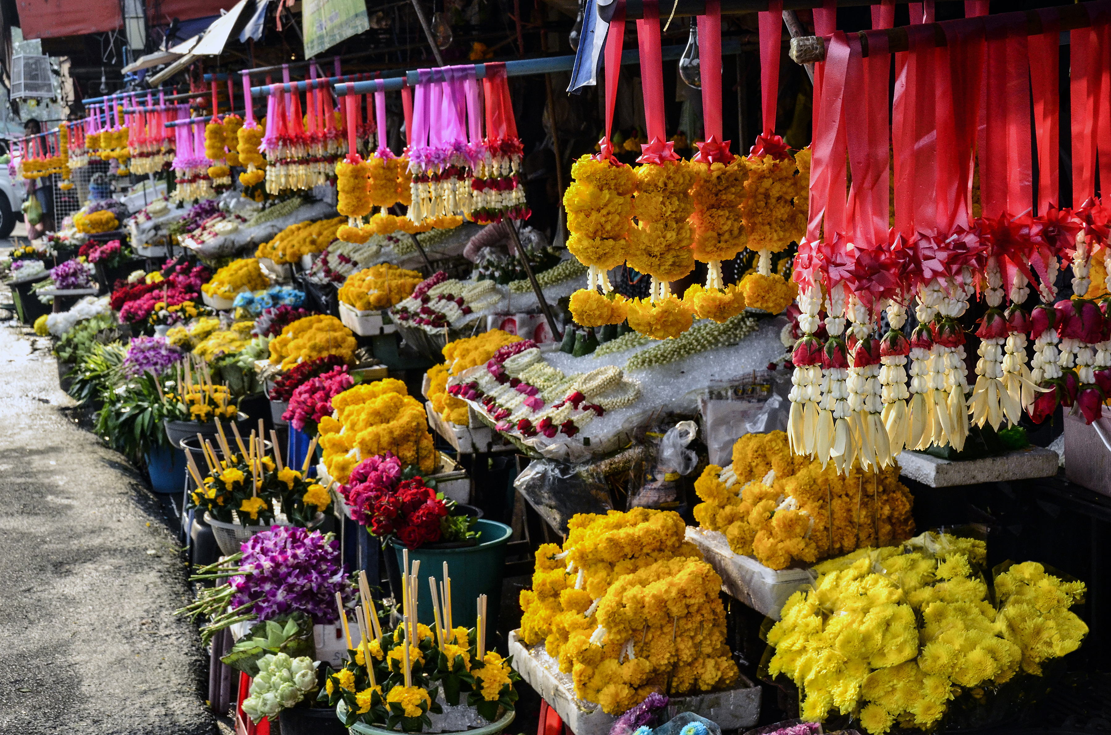 Colorful Thai flower market stall with hanging jasmine and marigold garlands.