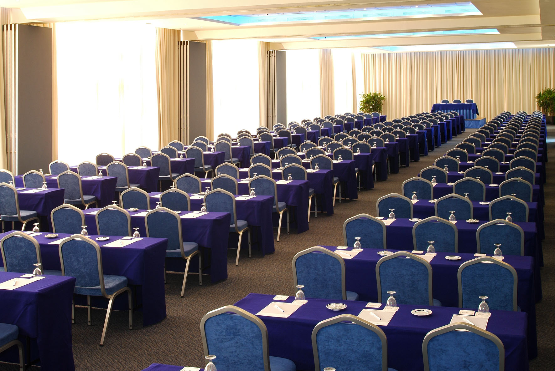 Large conference room with rows of blue tables and chairs, ready for an event.