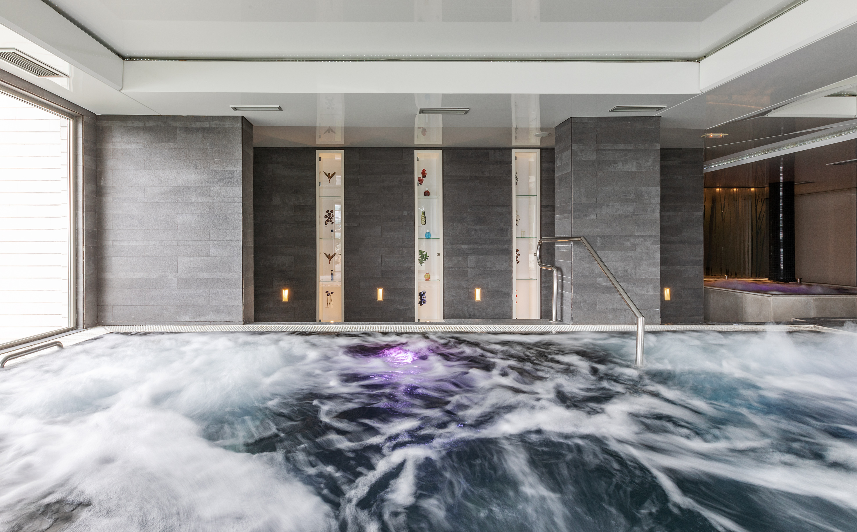 Bubbling spa hot tub, modern grey tiled walls, illuminated display.