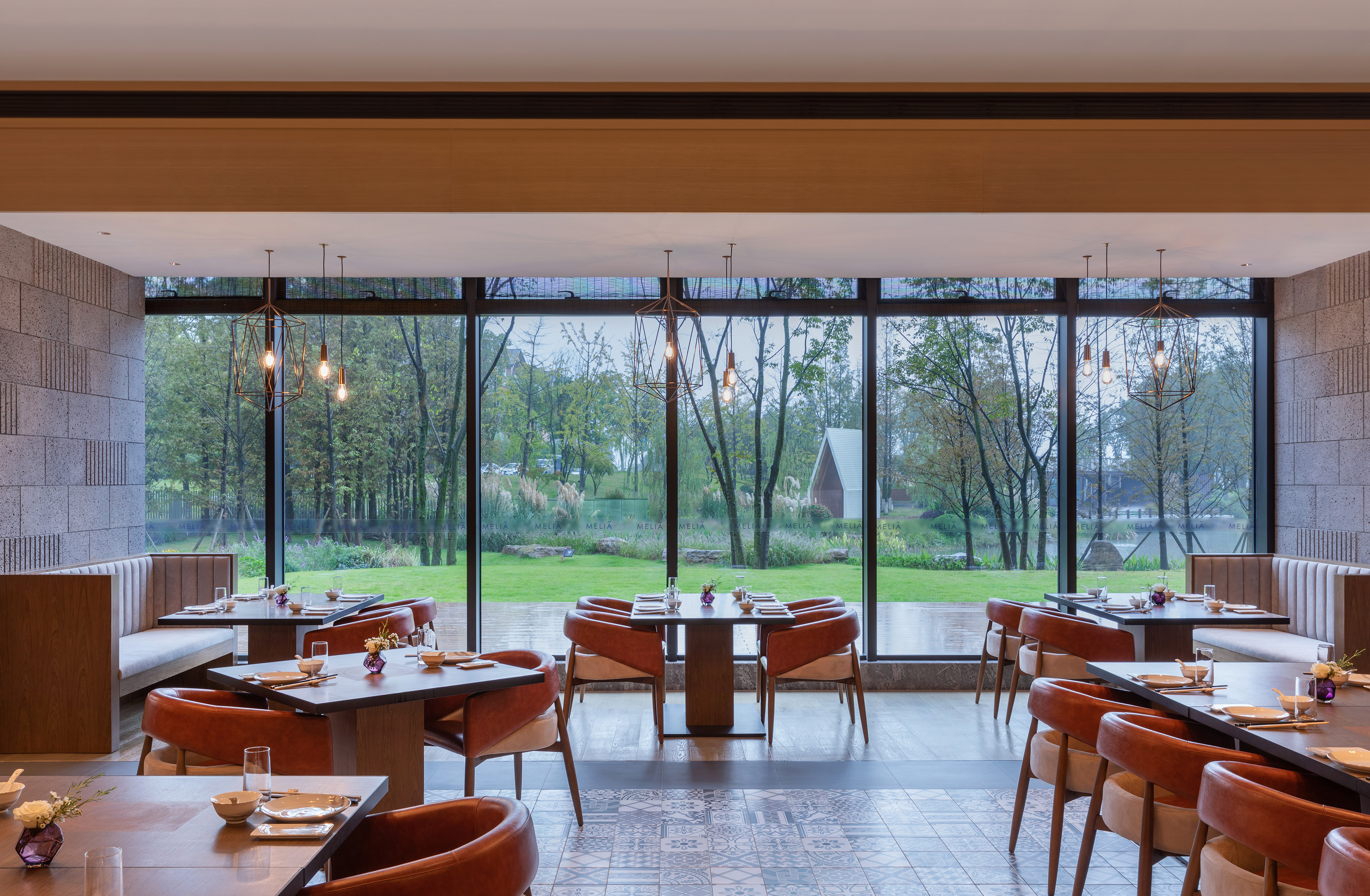 Modern dining room with set tables, brown leather chairs, and garden view windows.