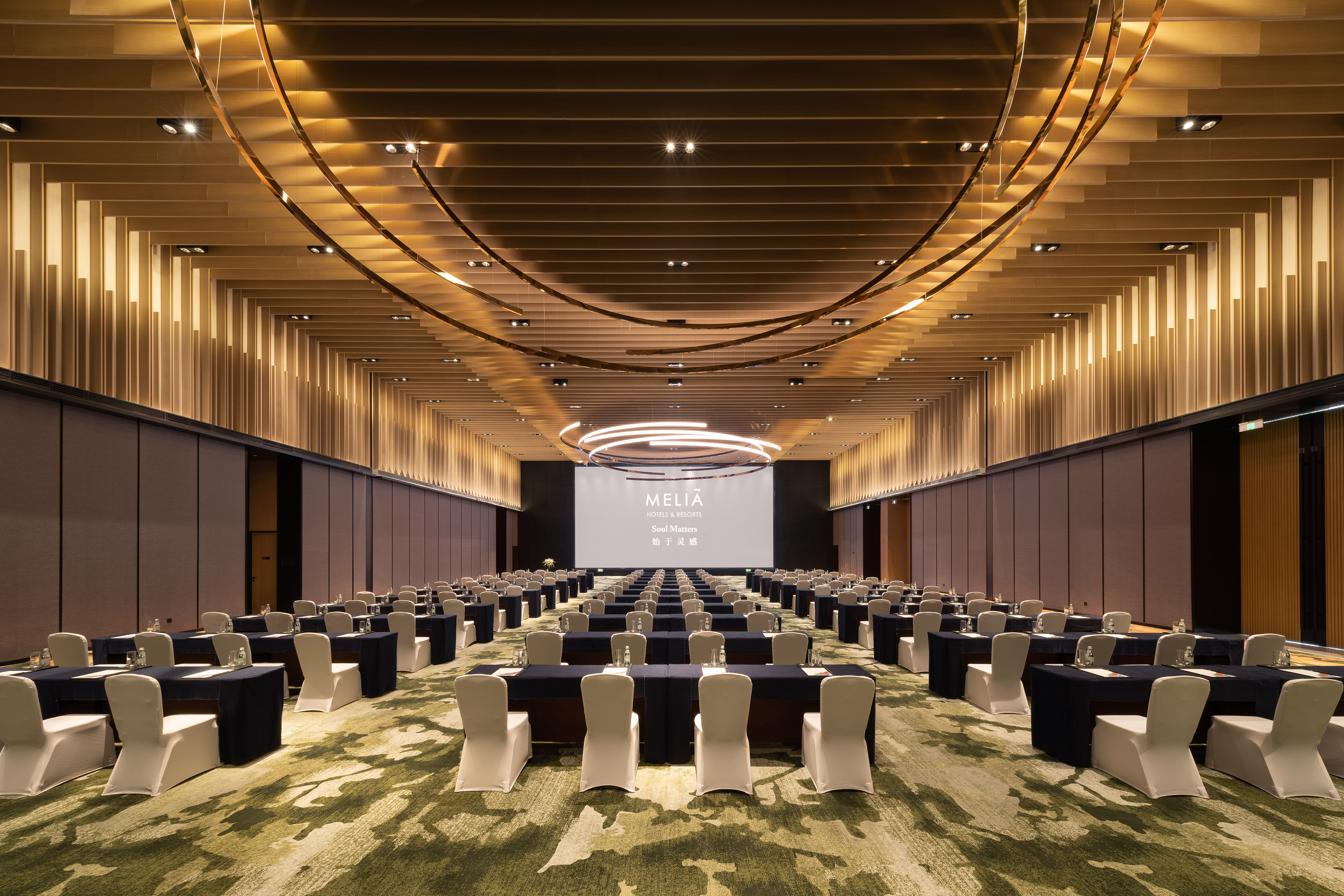 Meliá hotel conference ballroom, modern setup with tables, chairs, and screen.