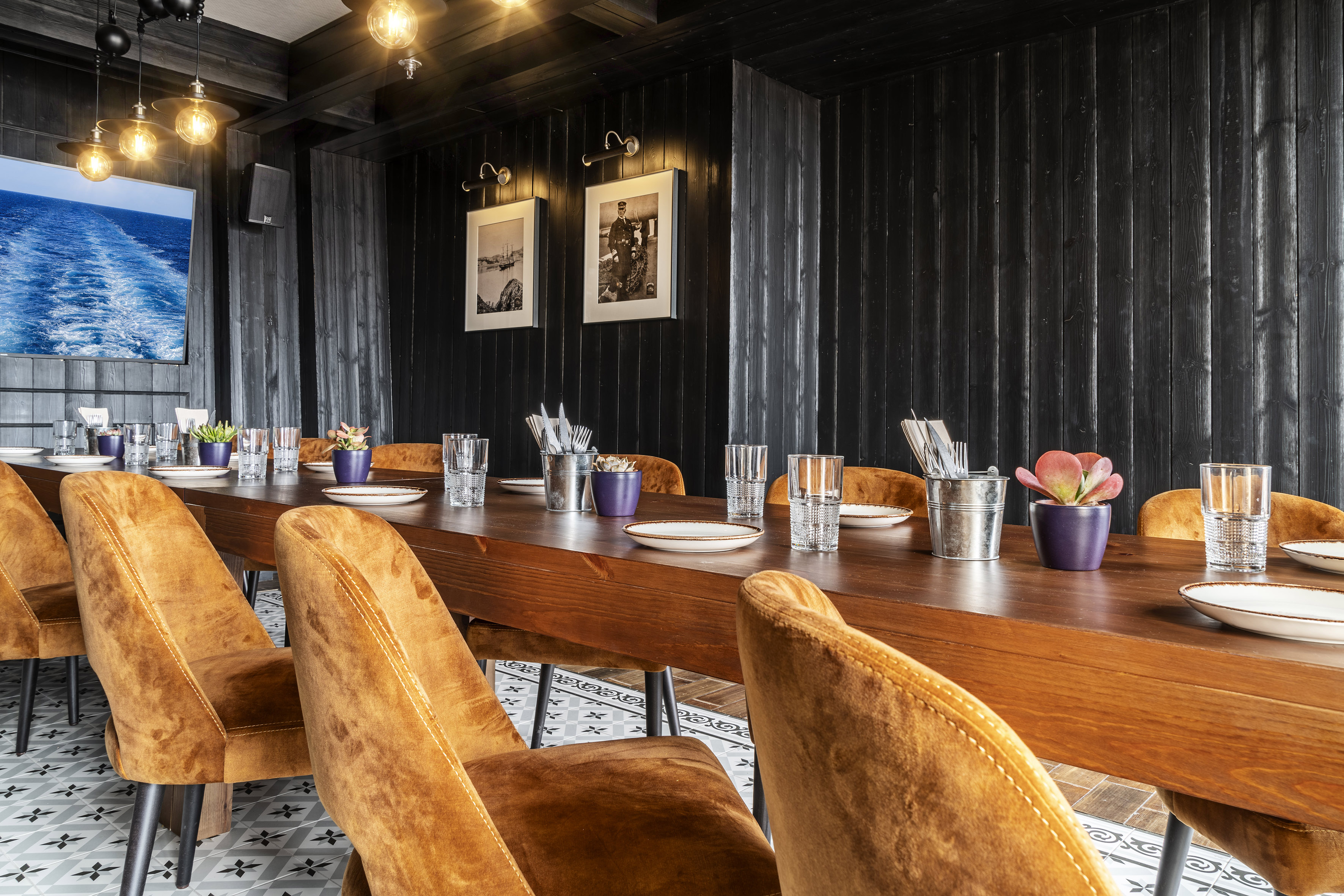 Nautical dining room: long wooden table, velvet chairs, black paneled walls.