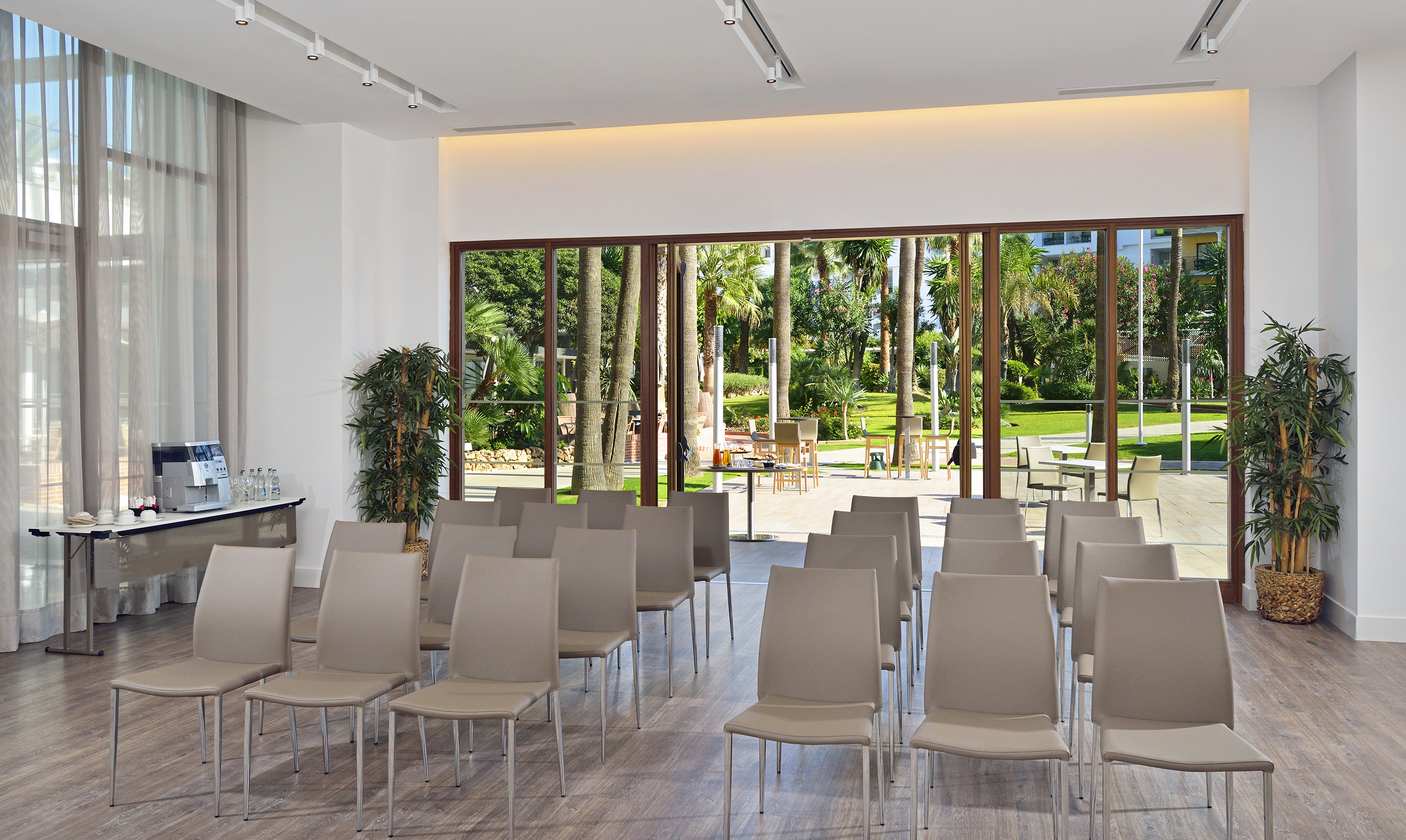 Hotel conference room with chairs, coffee station, and tropical garden view.