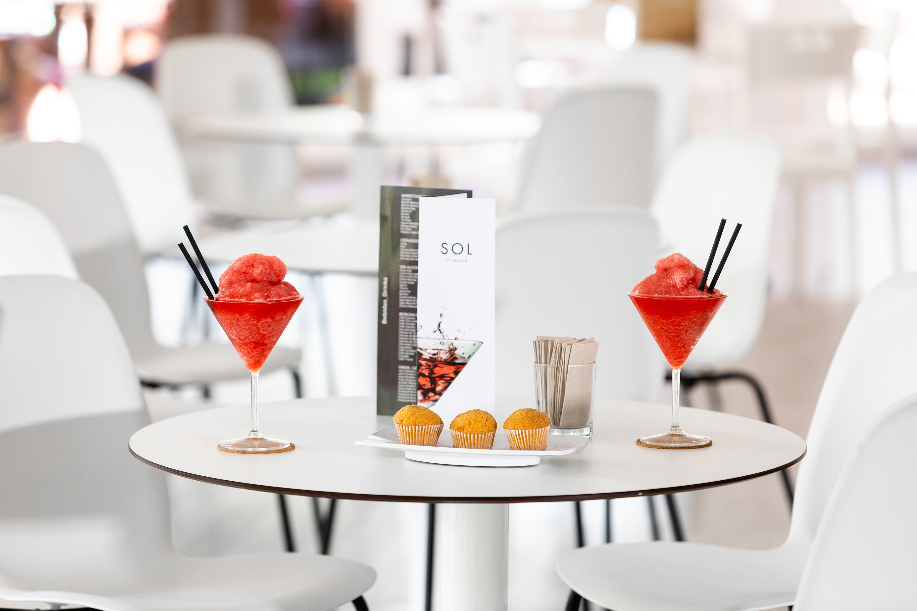Two red frozen drinks, muffins, and menu on a resort cafe table.