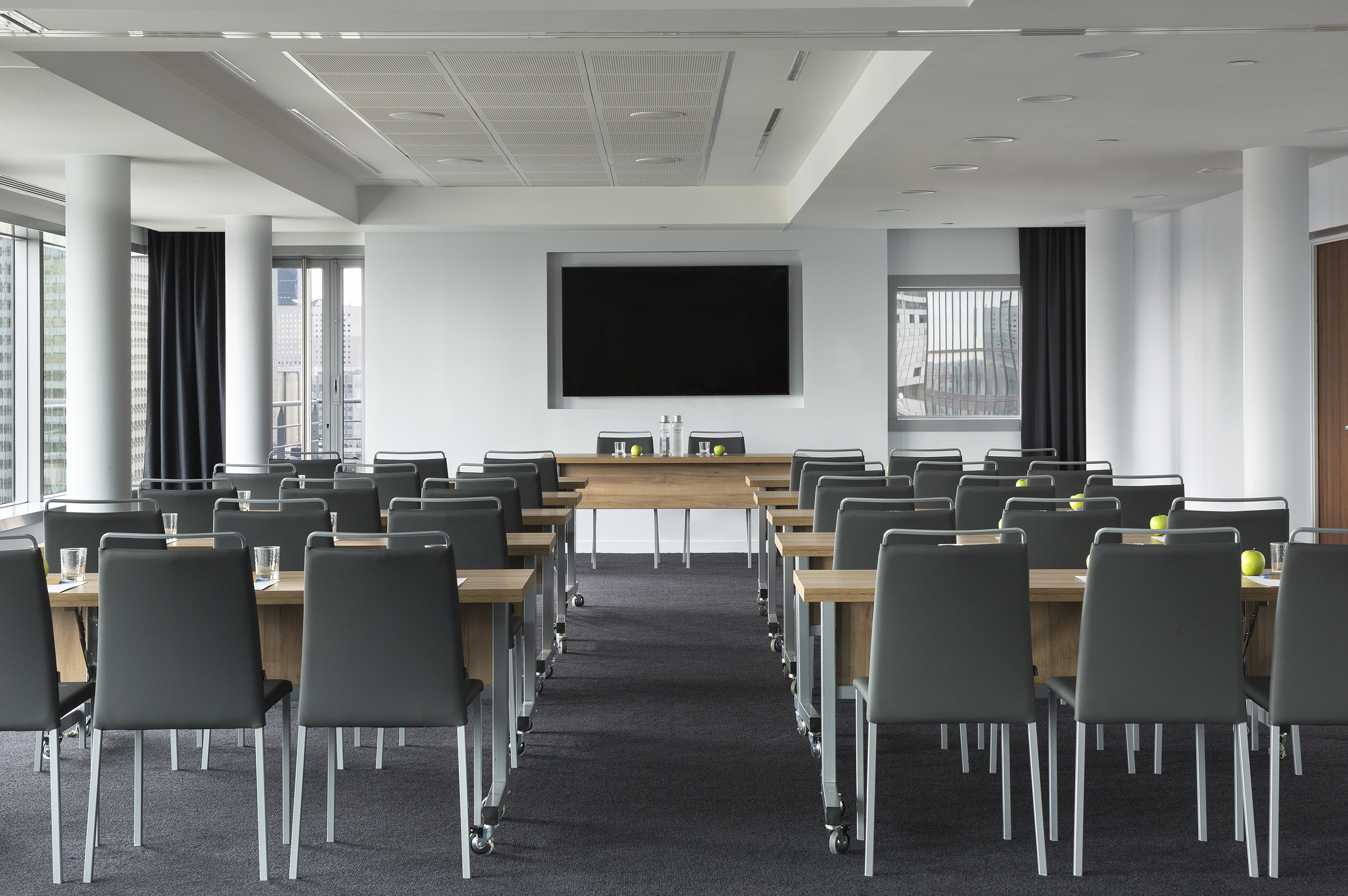 Modern conference room with classroom setup, large screen, and city view.