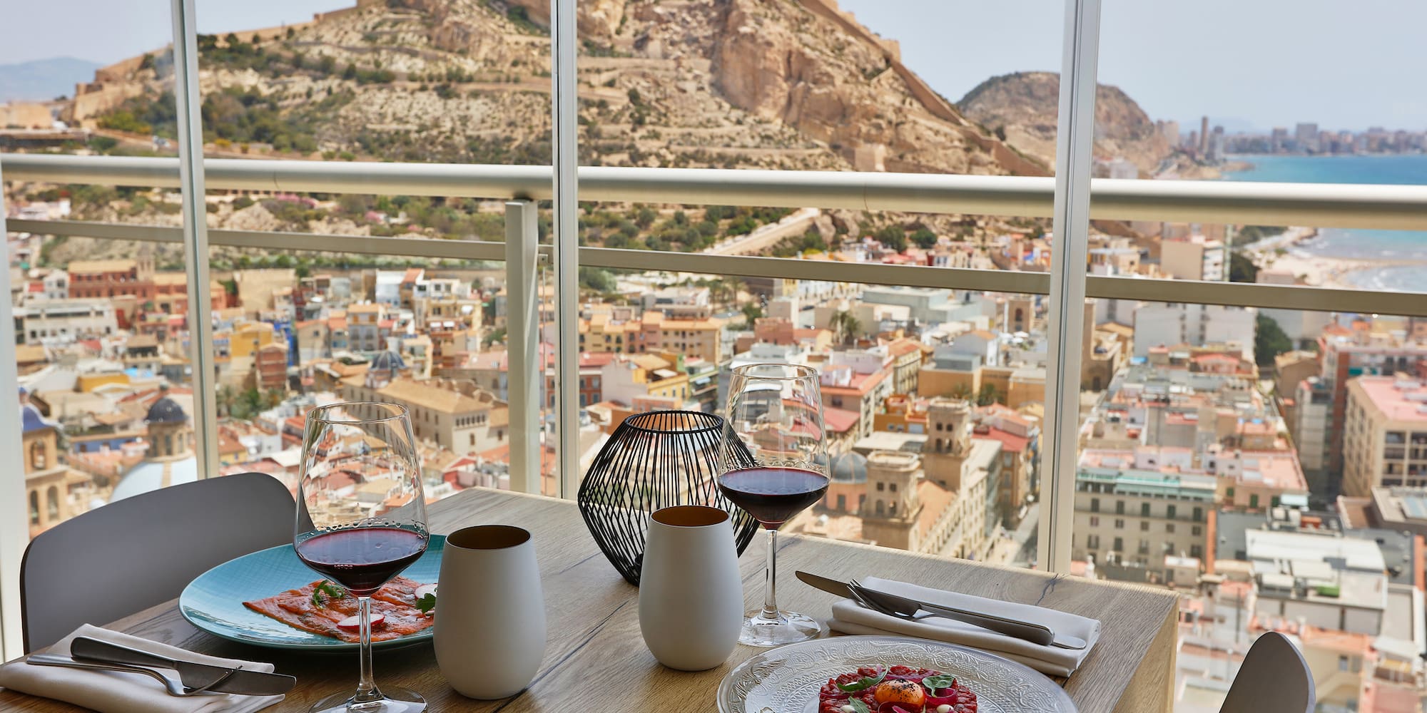 a table with plates of food and glasses on it with a view of a city