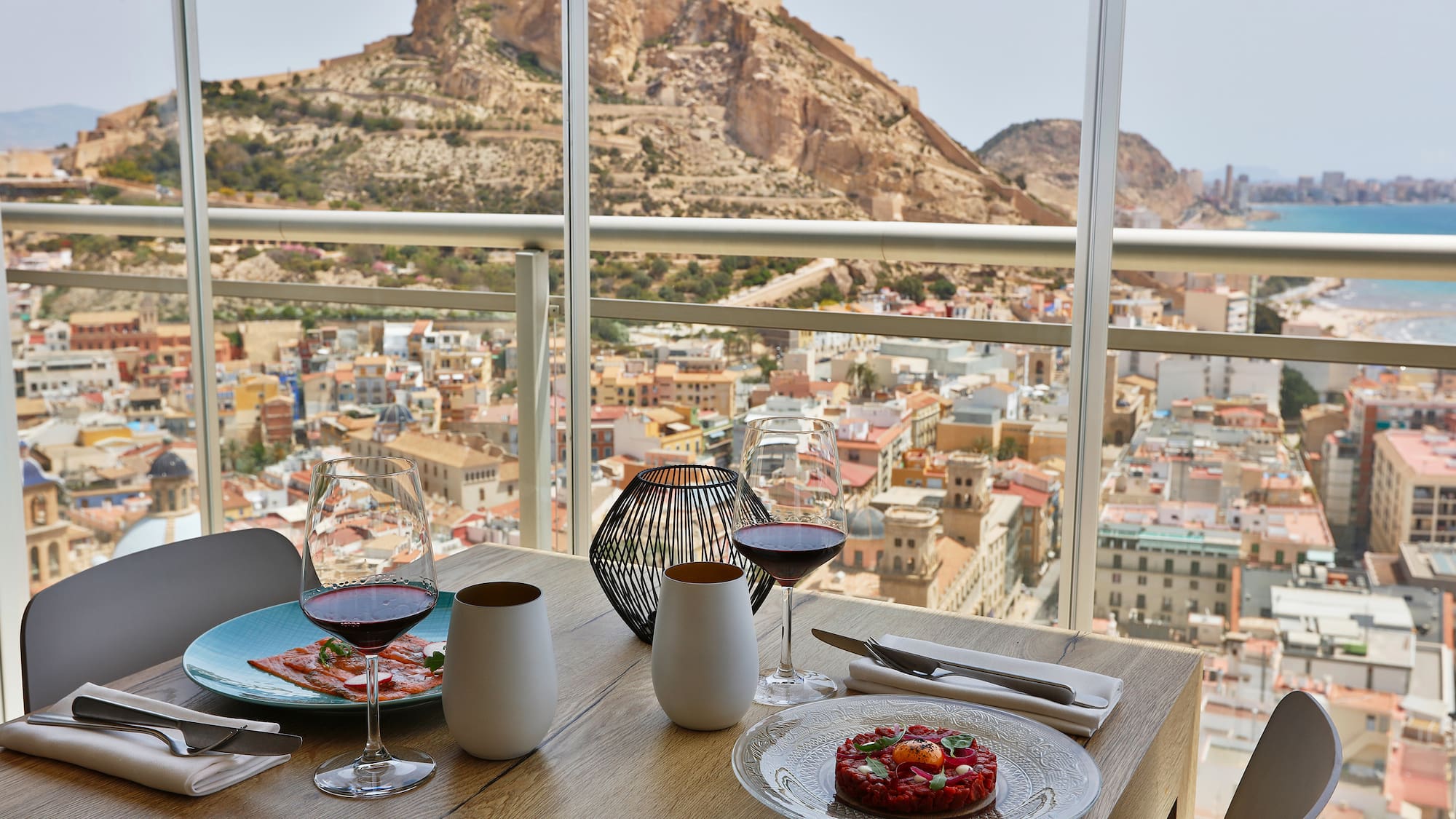 a table with plates of food and glasses on it with a view of a city