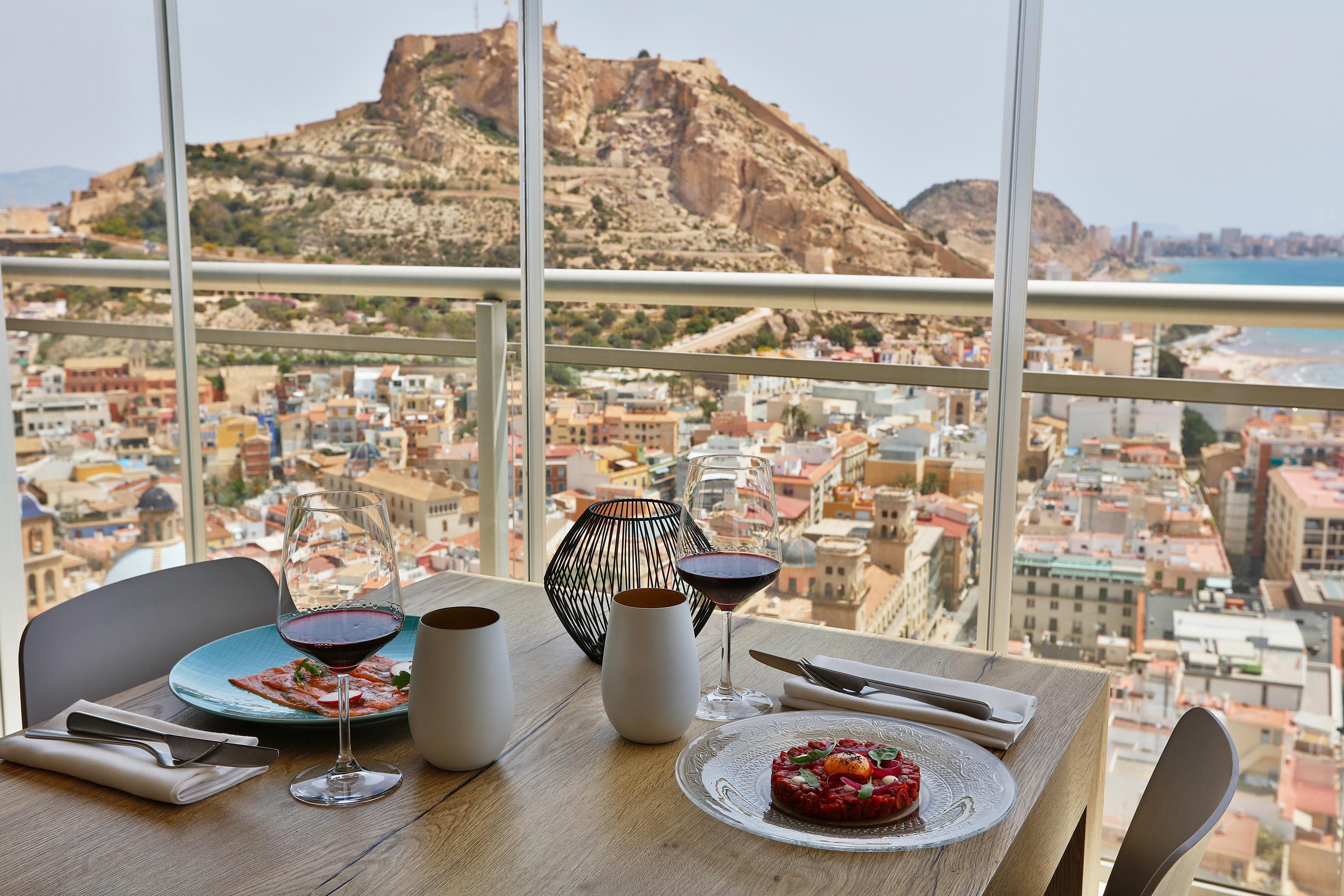 a table with plates of food and glasses on it with a view of a city