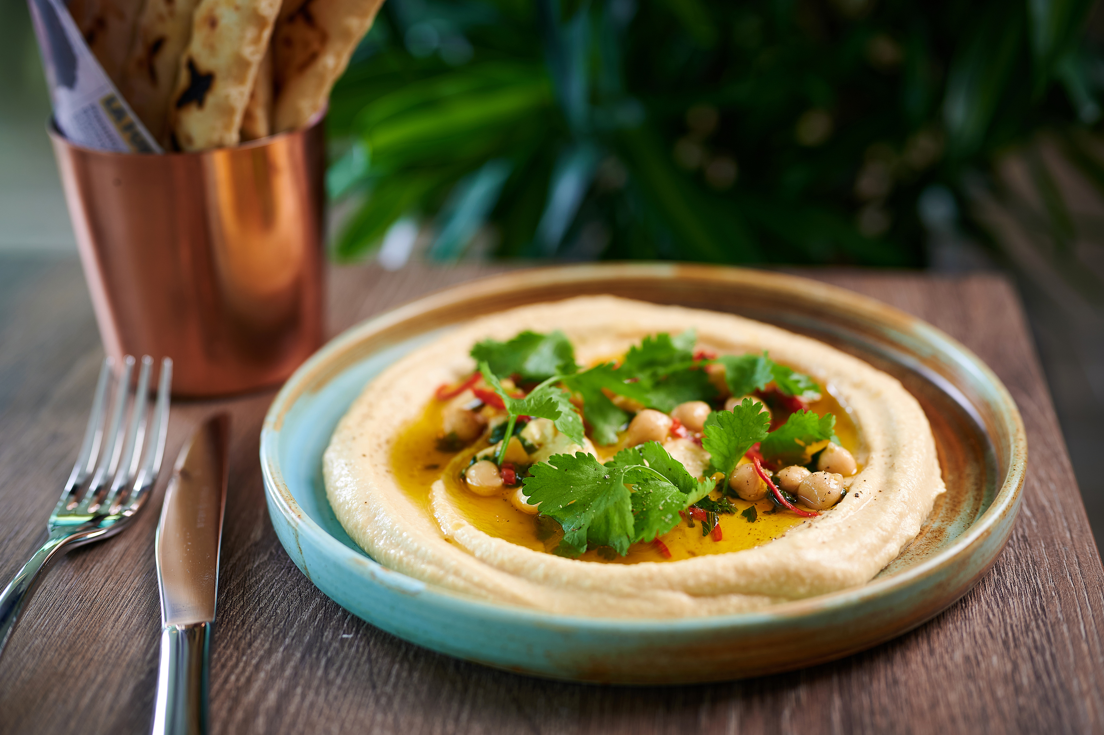 Creamy hummus topped with chickpeas, olive oil, cilantro, chili flakes, and flatbread.