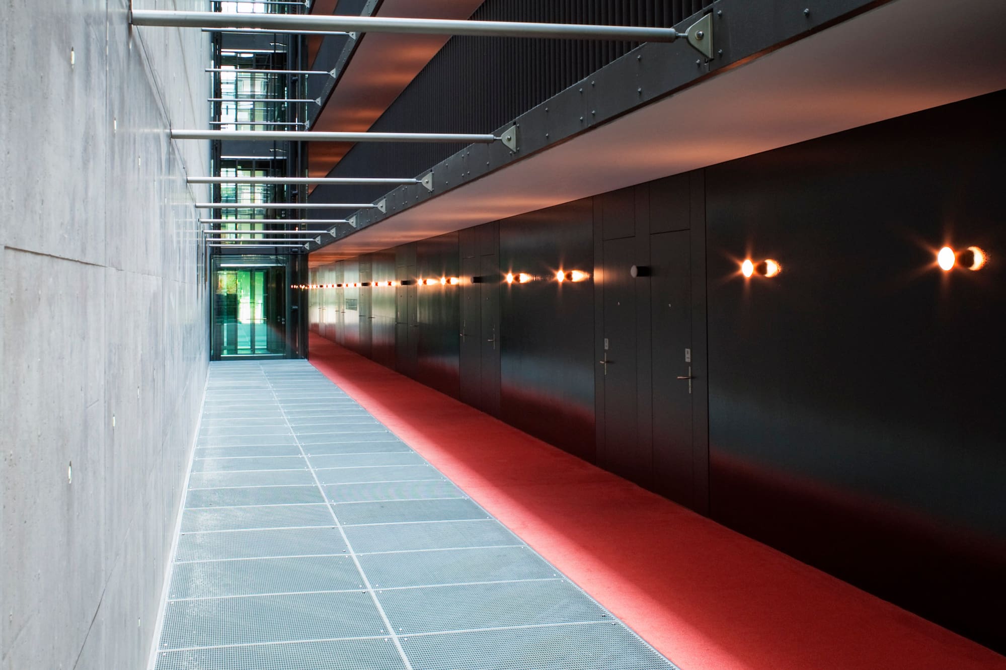 Modern corridor: concrete, metal grate floor, red carpet, and dark lit wall.
