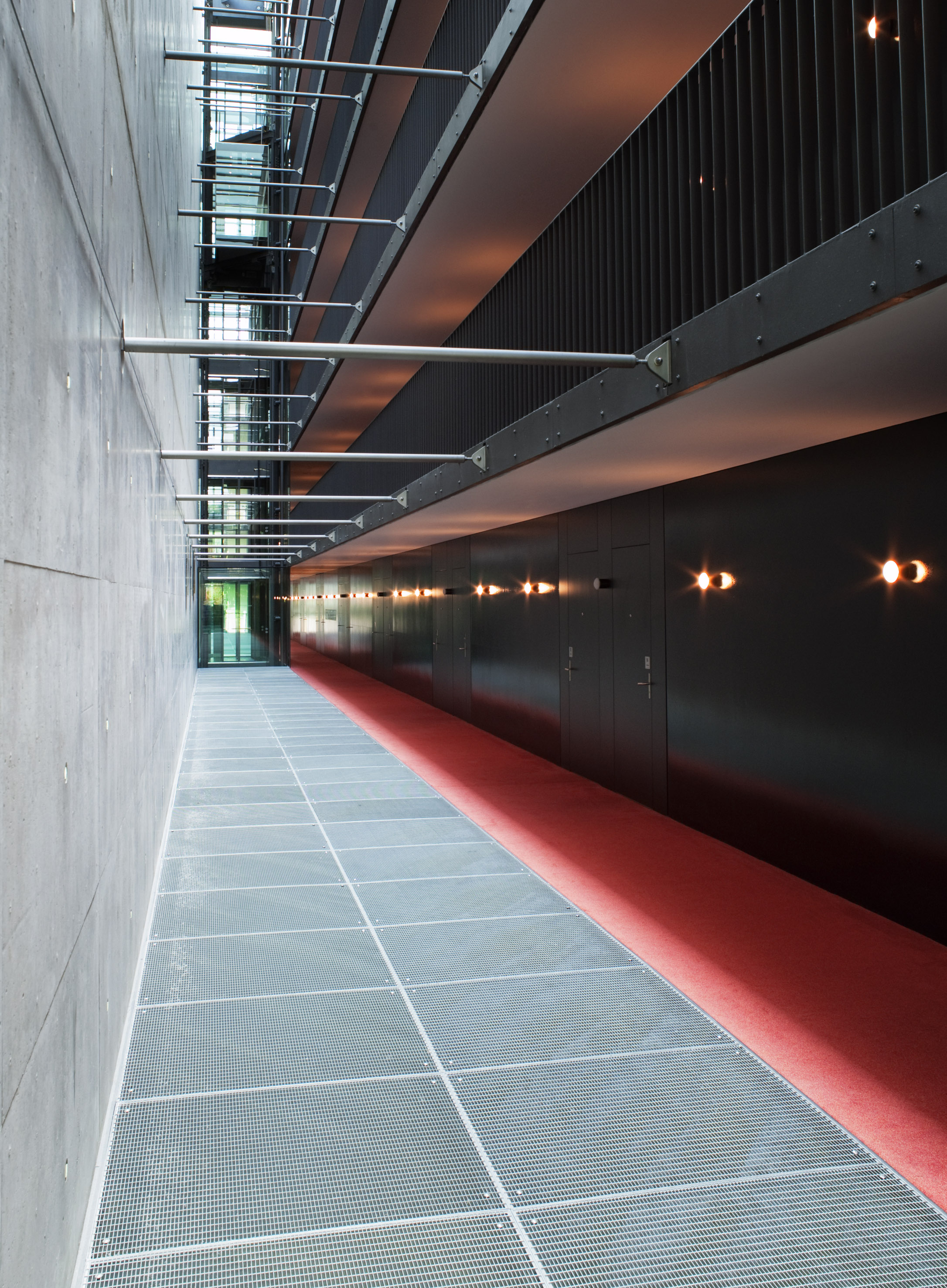 Modern corridor: concrete, metal grate floor, red carpet, and dark lit wall.