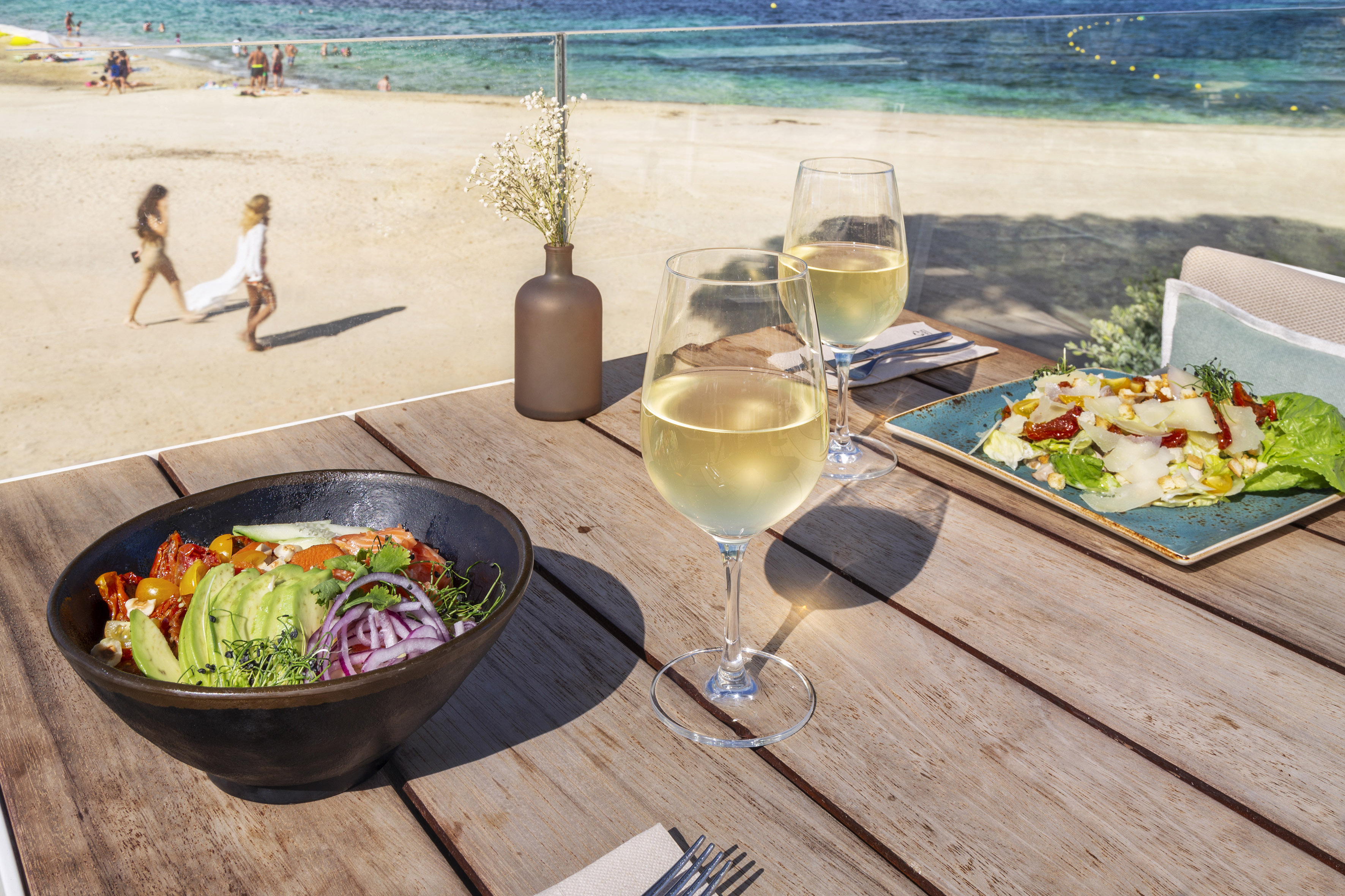 Beachfront dining with two salads, white wine, and ocean view.