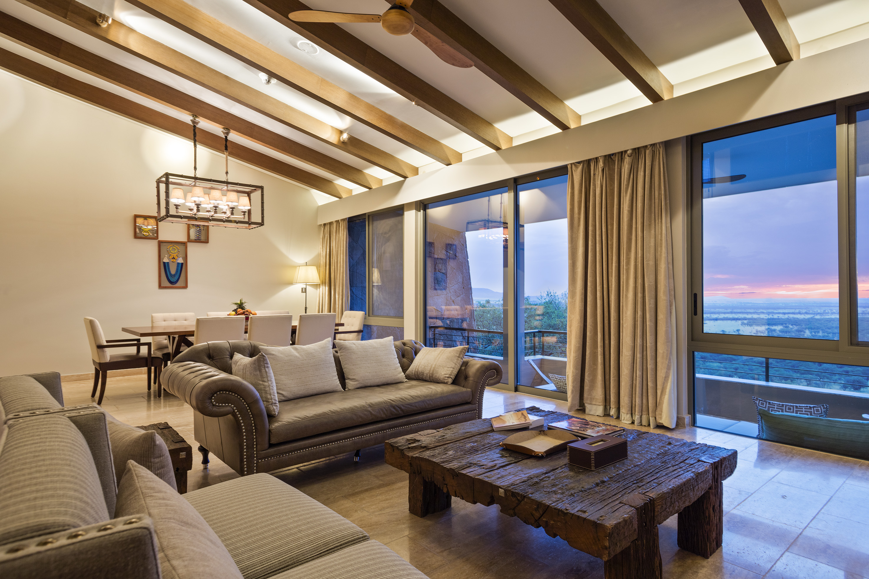 Modern luxury living room with panoramic view, rustic table, and wood beam ceiling.