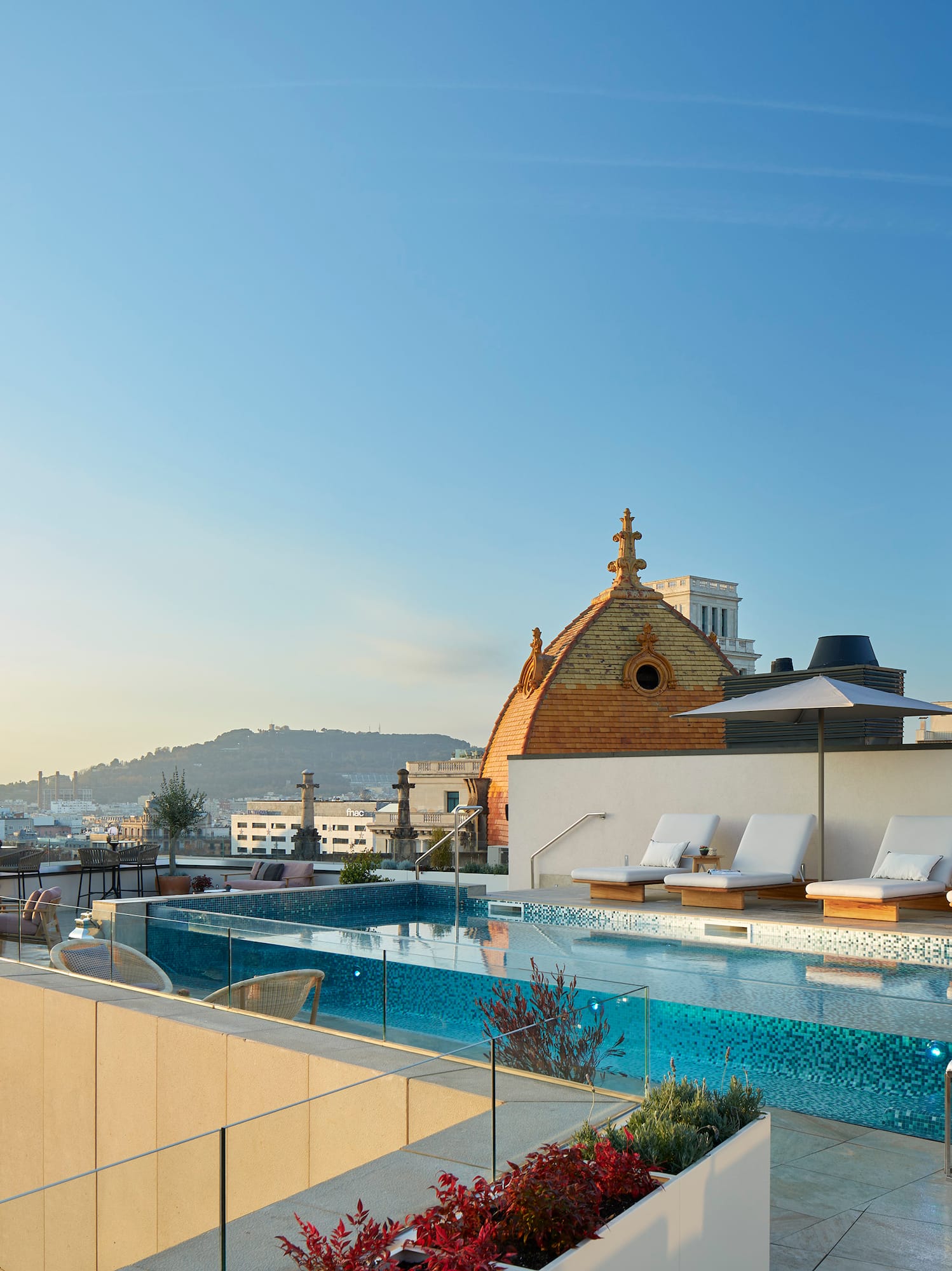 a pool with lounge chairs and a rooftop with a city in the background