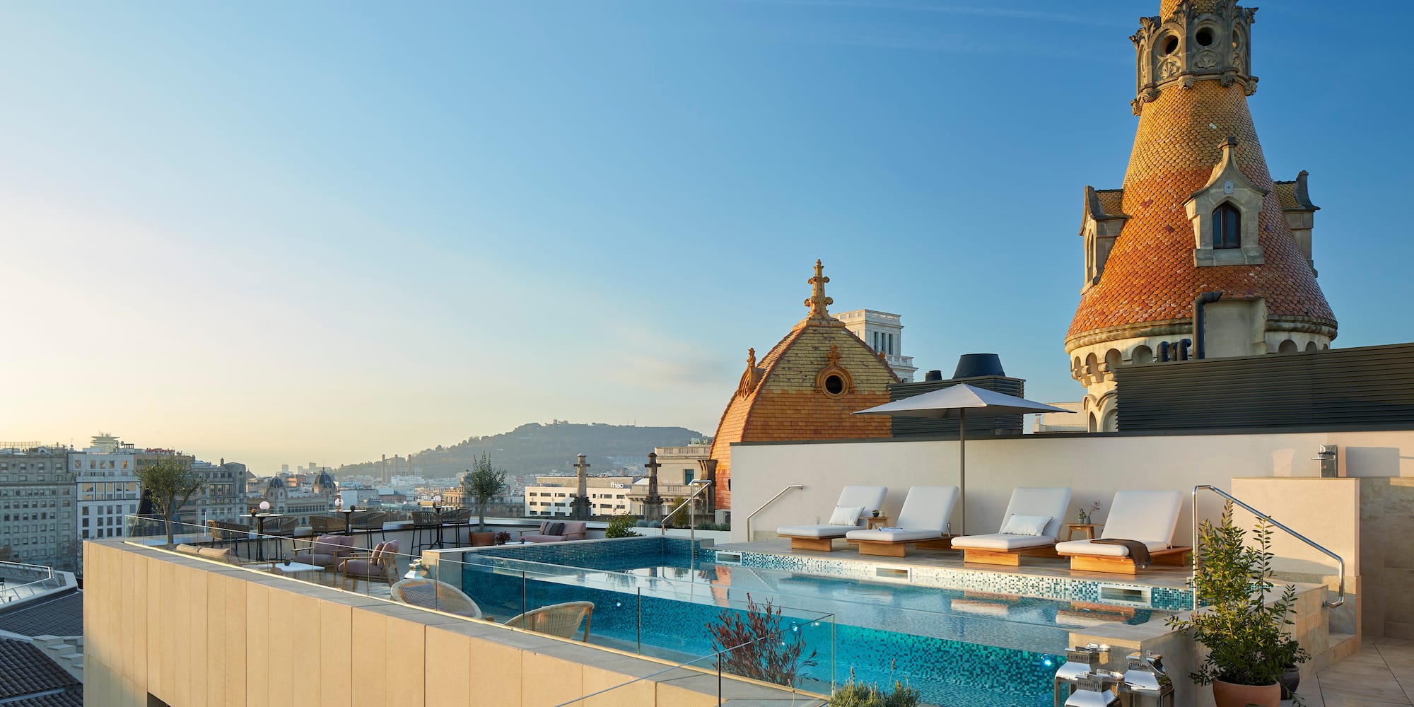 a pool with lounge chairs and a rooftop with a city in the background