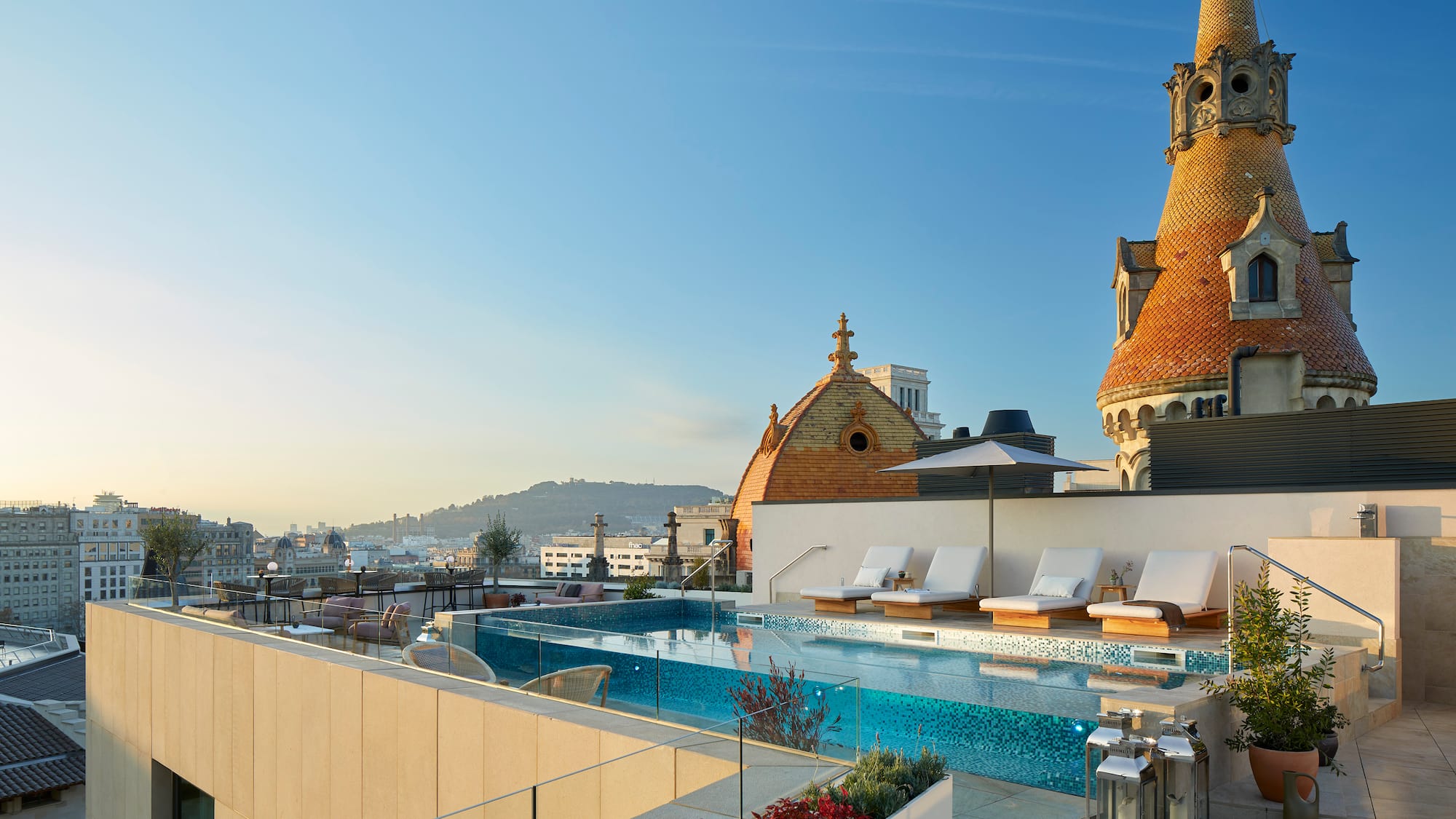 a pool with lounge chairs and a rooftop with a city in the background