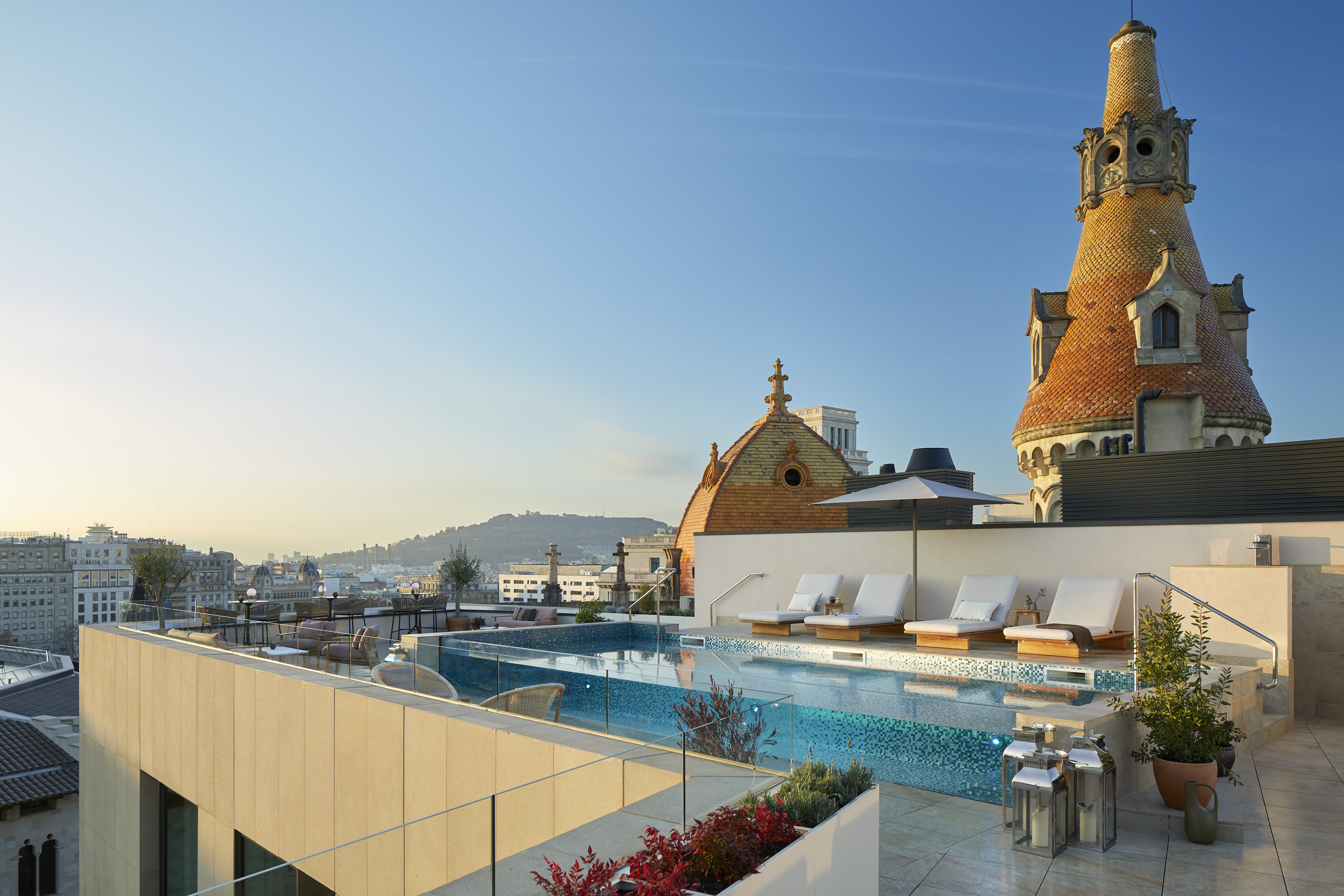 a pool with lounge chairs and a rooftop with a city in the background