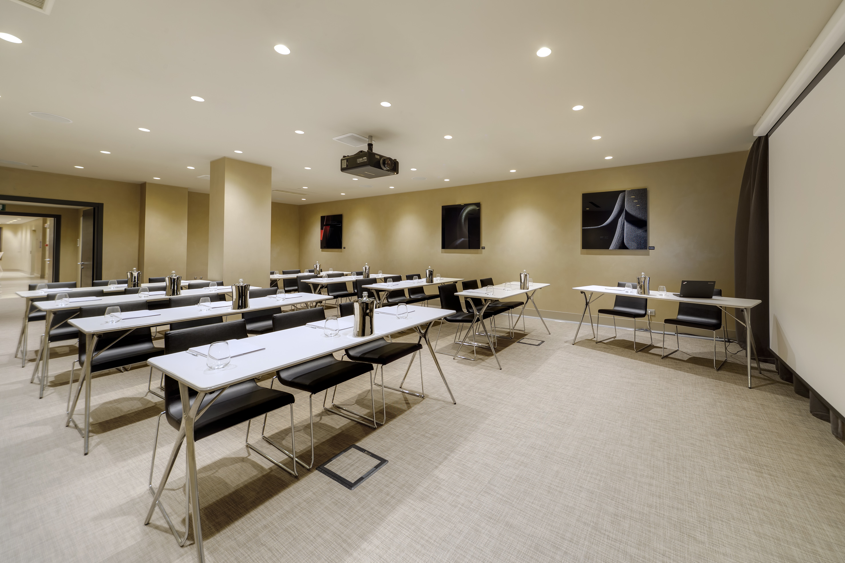 Empty corporate meeting room with projector, screen, and rows of tables.