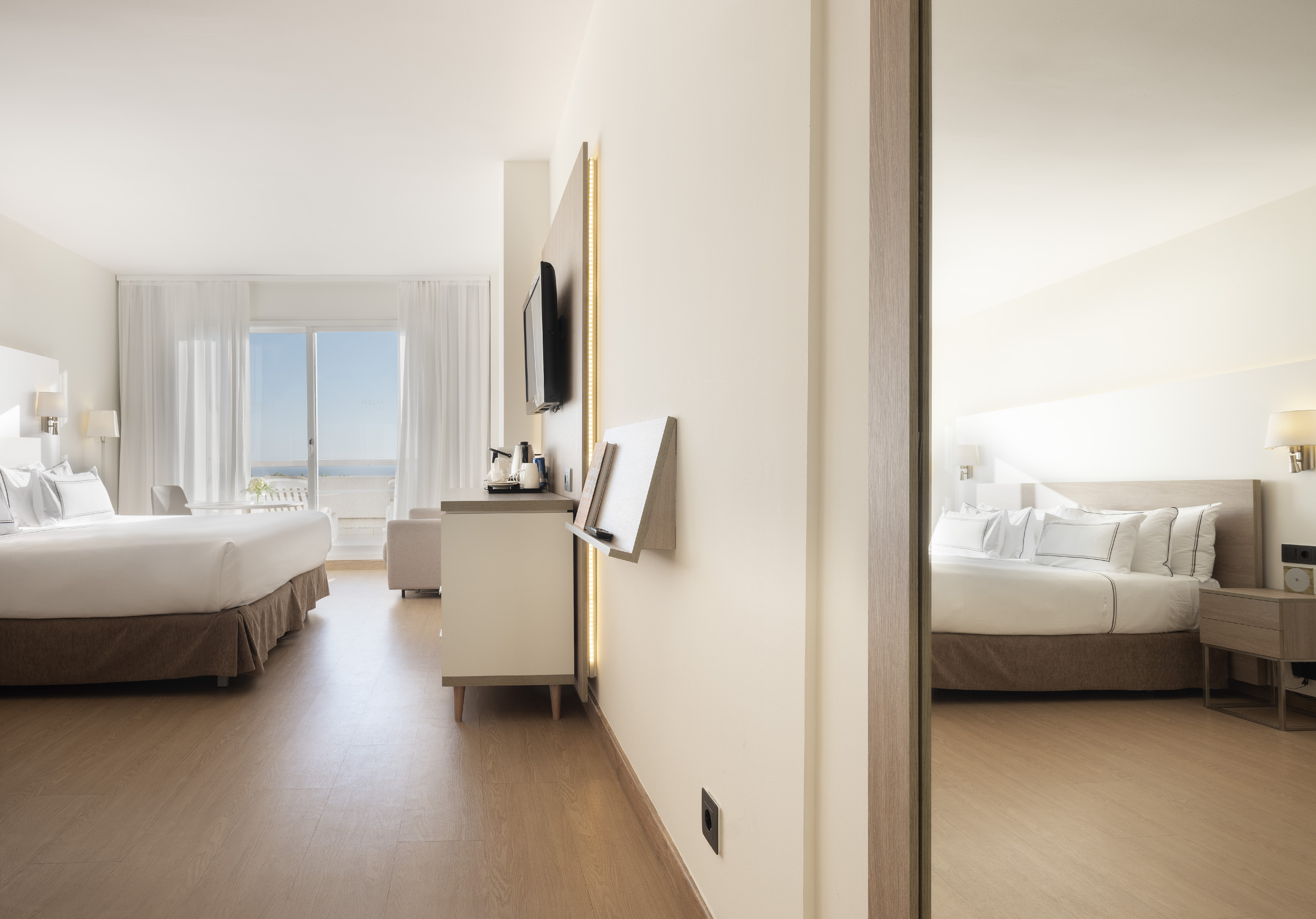 Bright hotel suite with ocean view balcony, king bed, and modern white decor.
