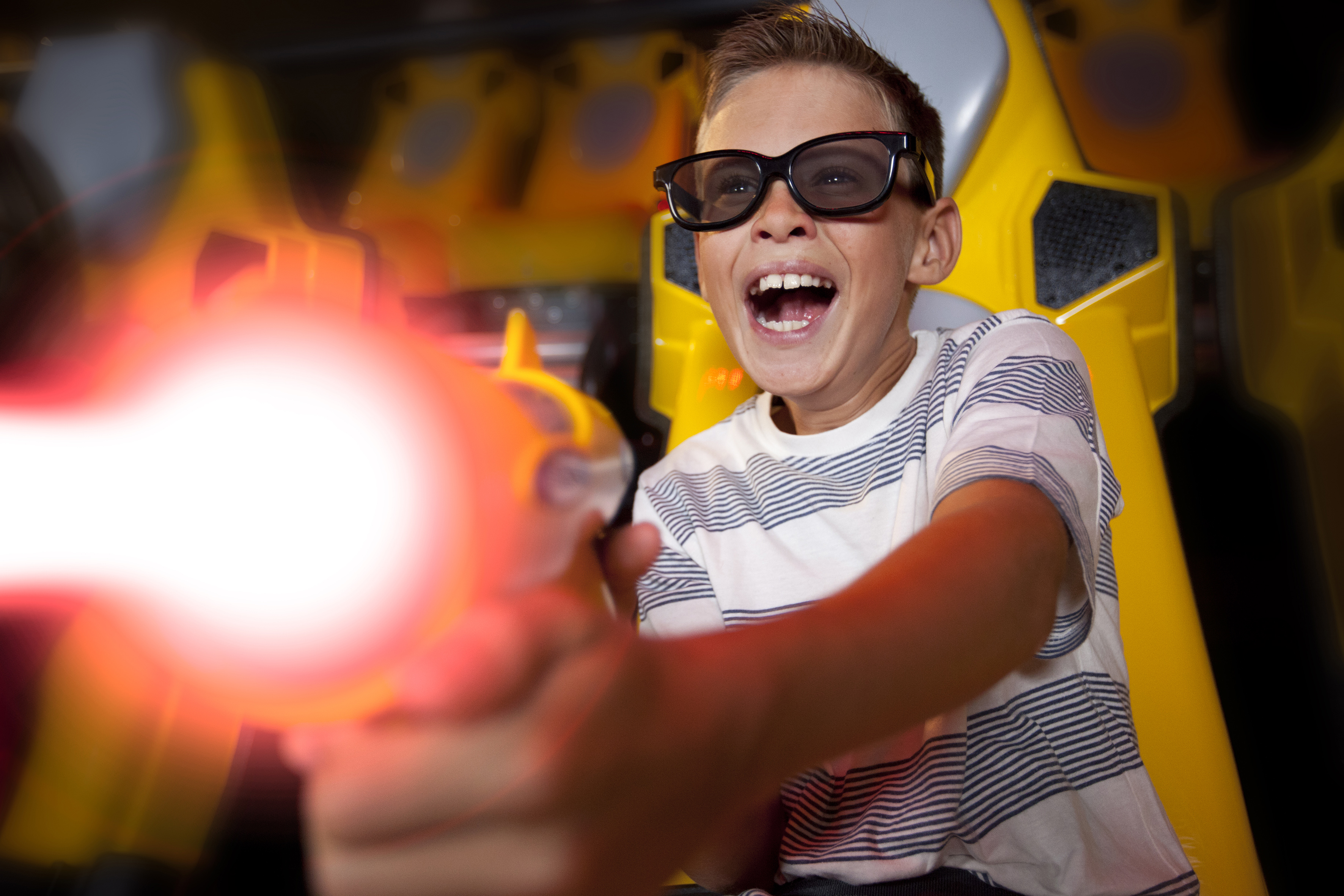 Thrilled boy in 3D glasses plays arcade shooter with glowing laser gun.