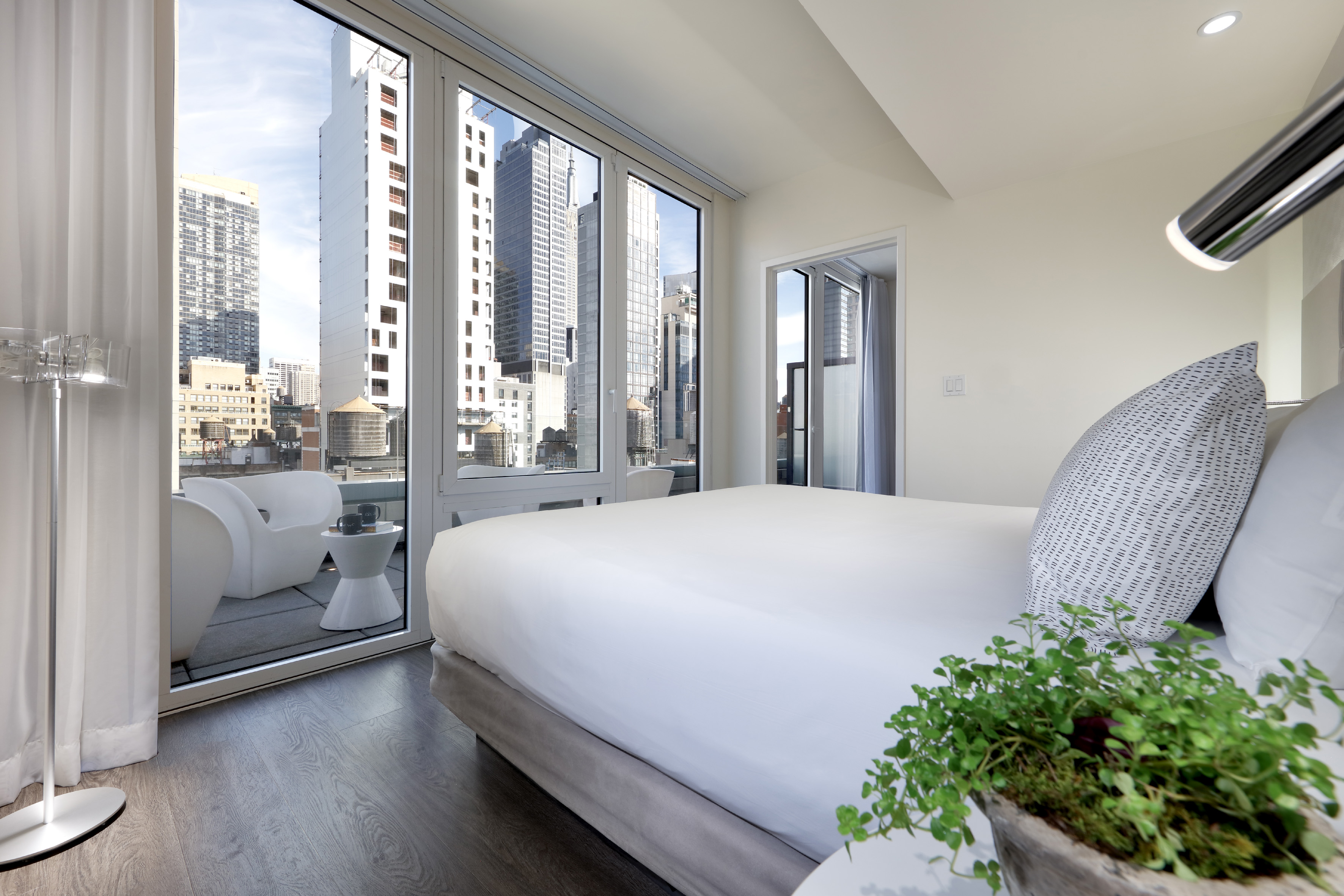 Modern hotel room with NYC skyline view, large windows, and balcony.