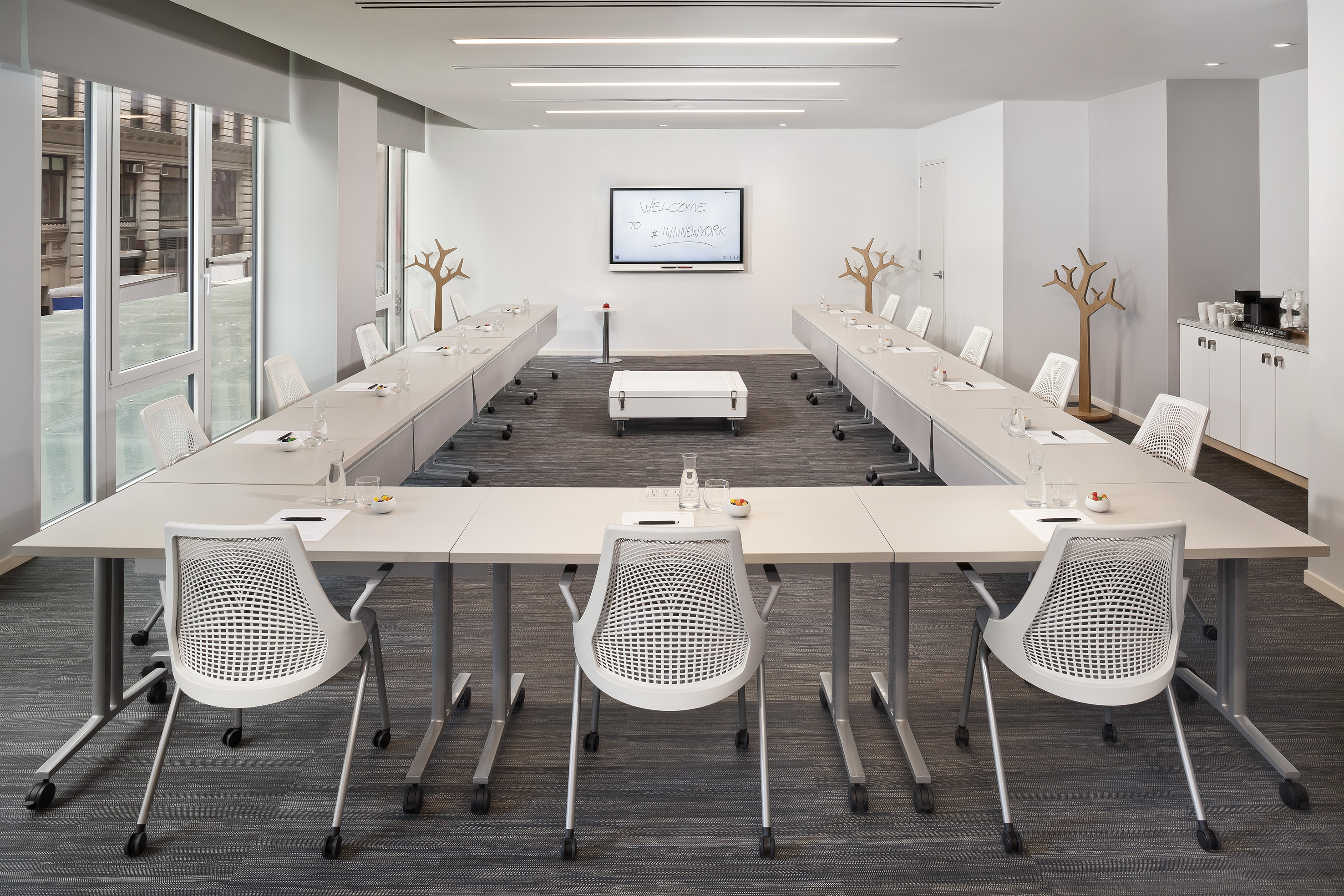 Modern U-shaped conference room, white chairs, digital display, natural light.
