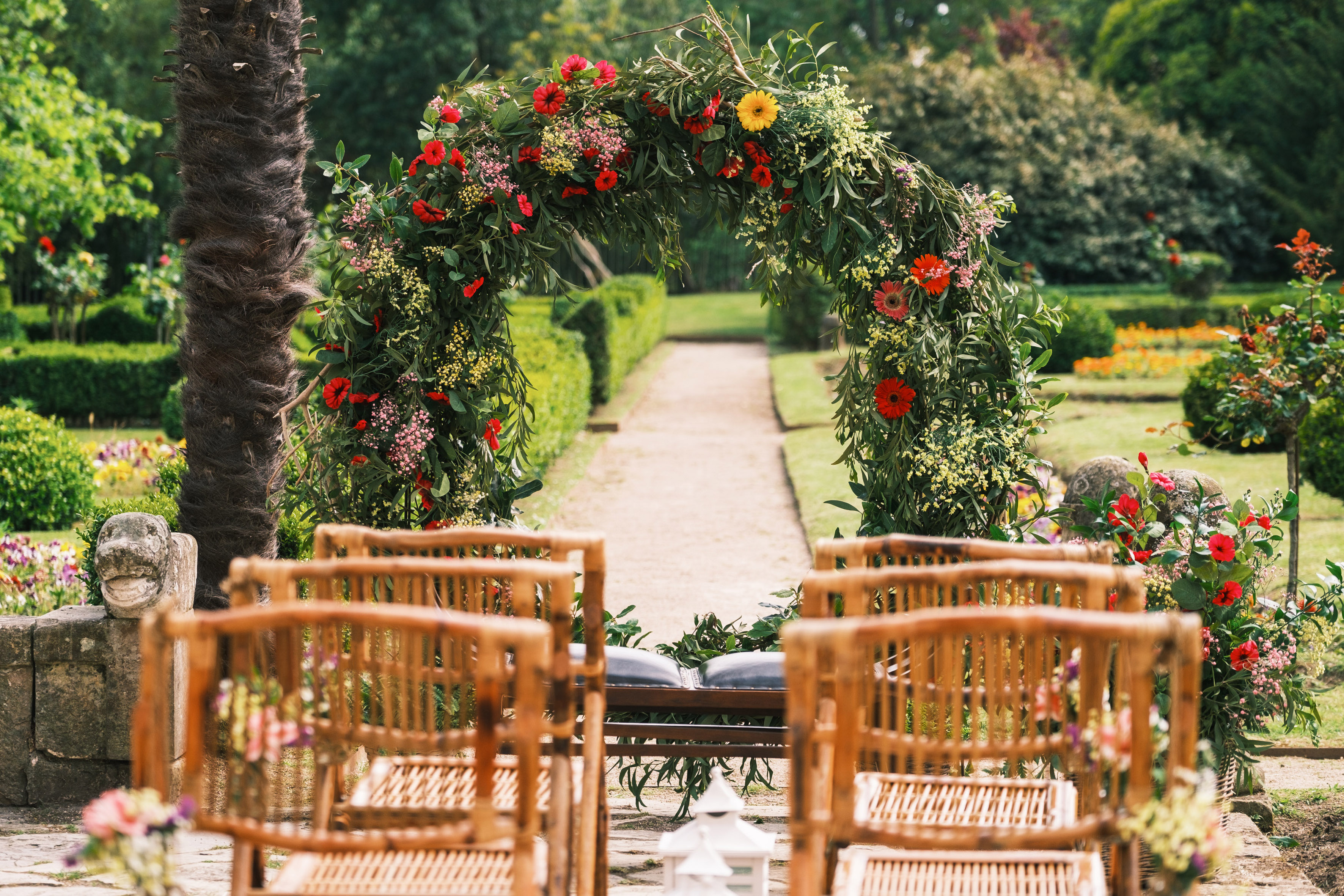 Garden wedding ceremony aisle with floral arch and wooden chairs.