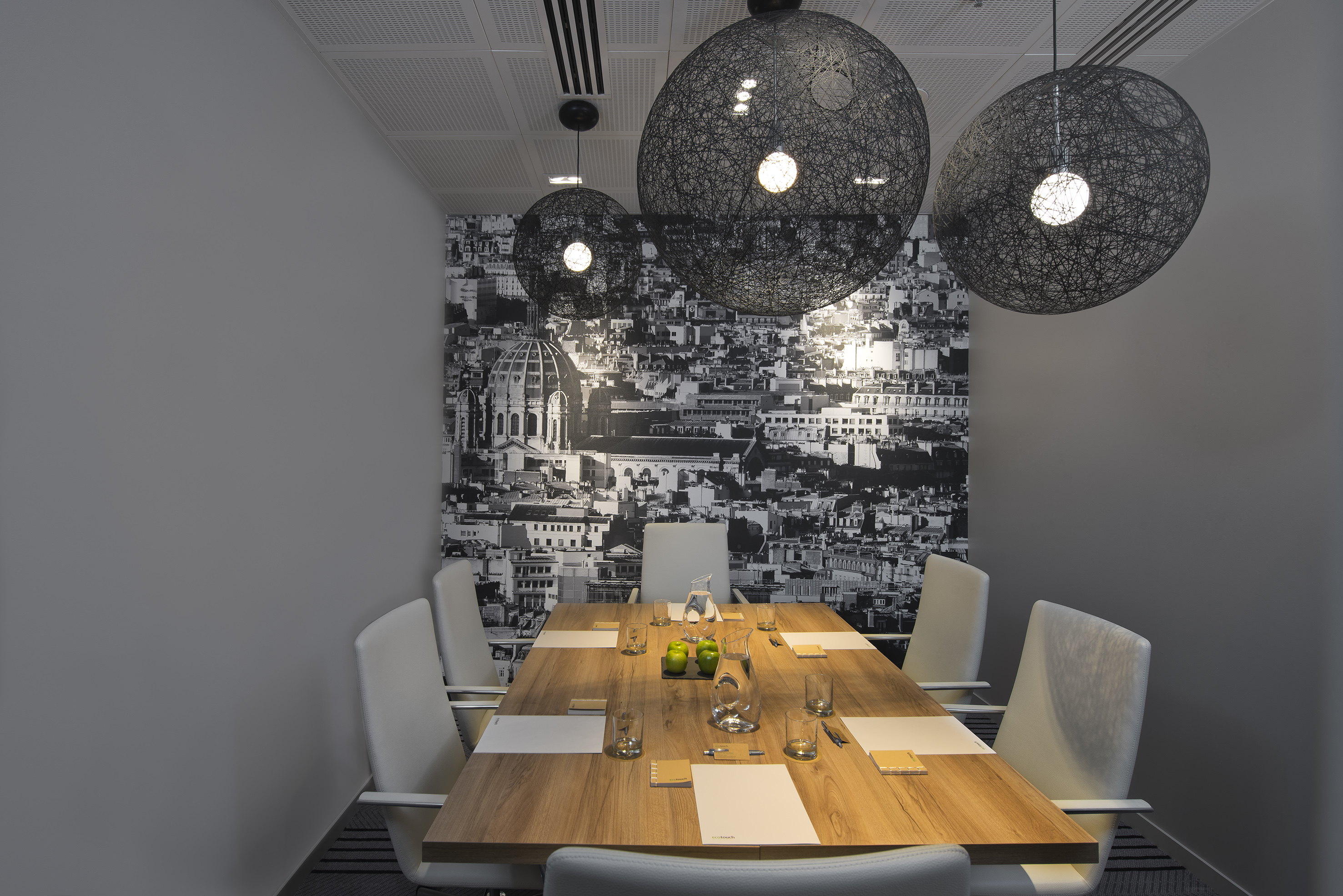 Modern boardroom with wooden table, white chairs, city mural, and pendant lights.