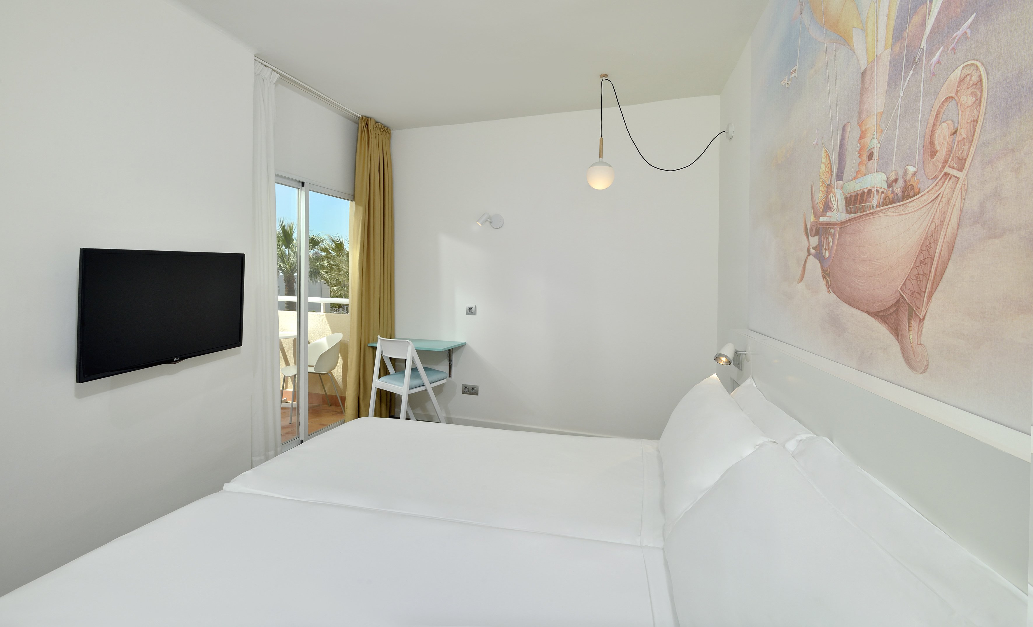 Modern hotel room with white bed, balcony, TV, and unique flying ship mural.