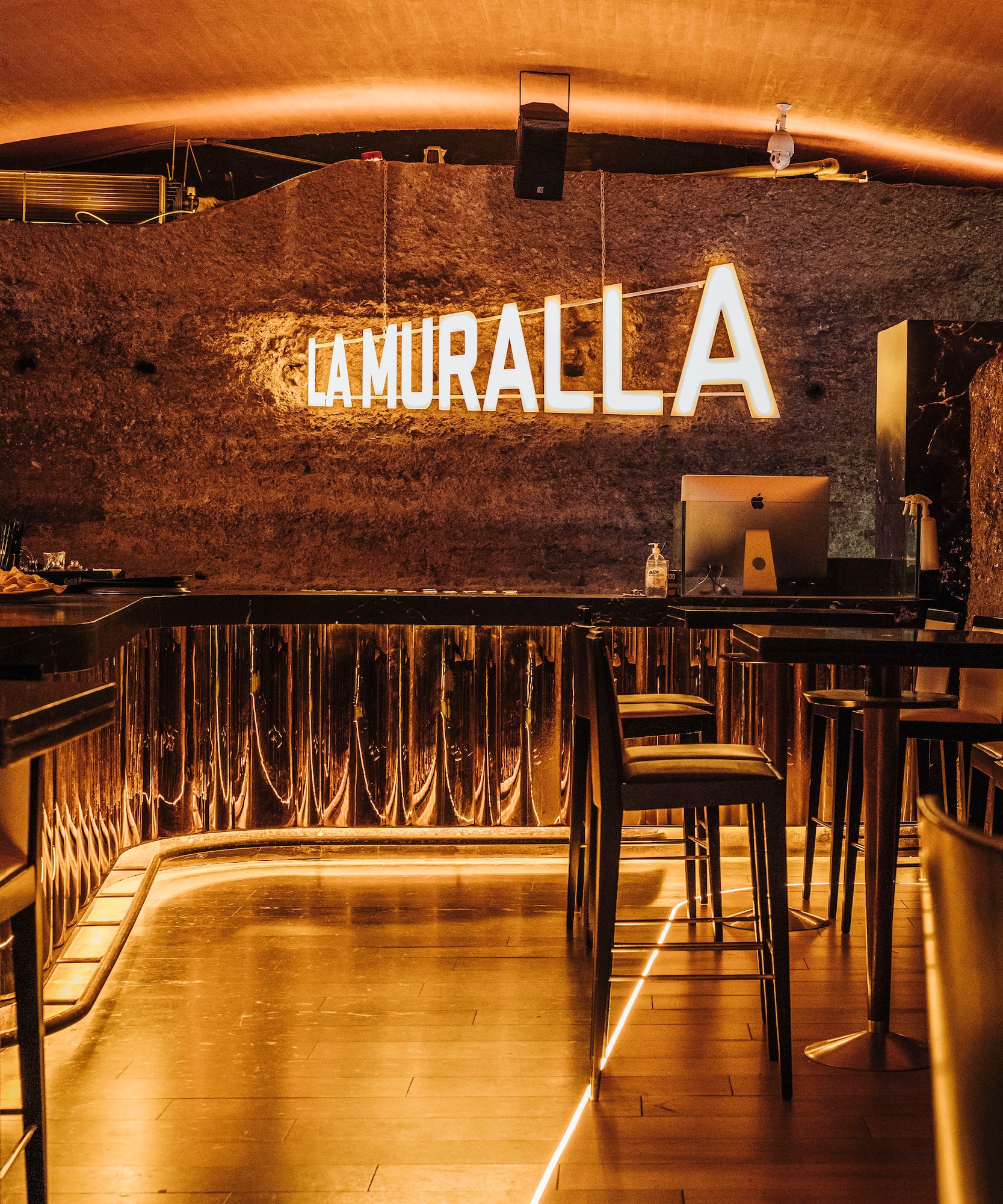 LA MURALLA bar: neon sign on textured wall, warm lighting, modern counter, and stools.