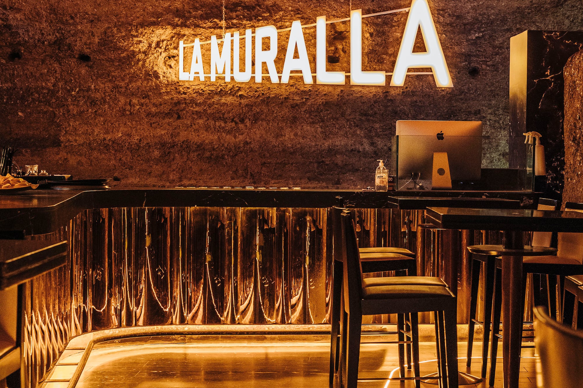 LA MURALLA bar: Neon sign, rock wall, warm lighting, modern interior design.
