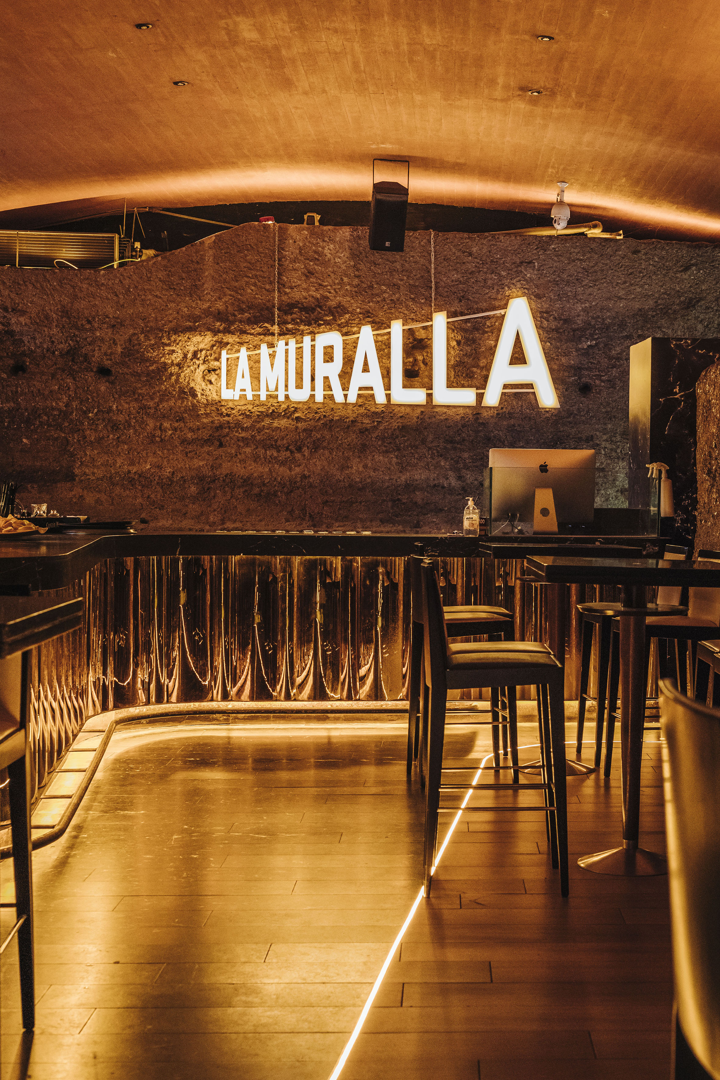 LA MURALLA bar: neon sign on textured wall, warm lighting, modern counter, and stools.