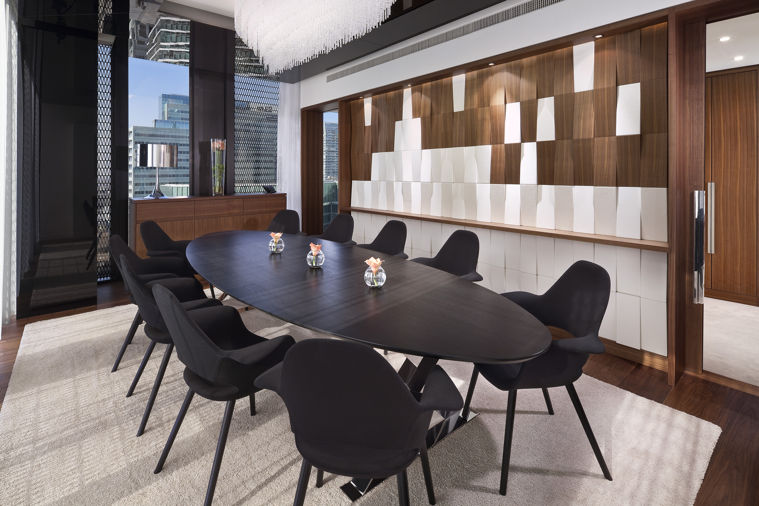 Luxury boardroom with modern oval table, black chairs, and city skyline view.