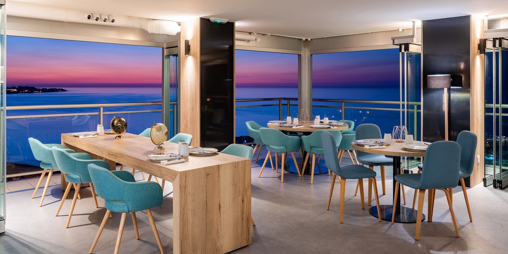 a room with a table and chairs and a balcony overlooking the ocean