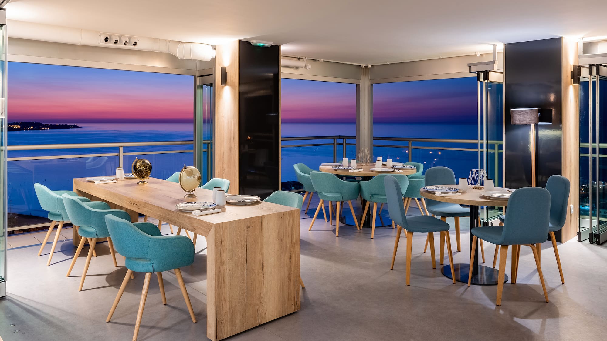 a room with a table and chairs and a balcony overlooking the ocean