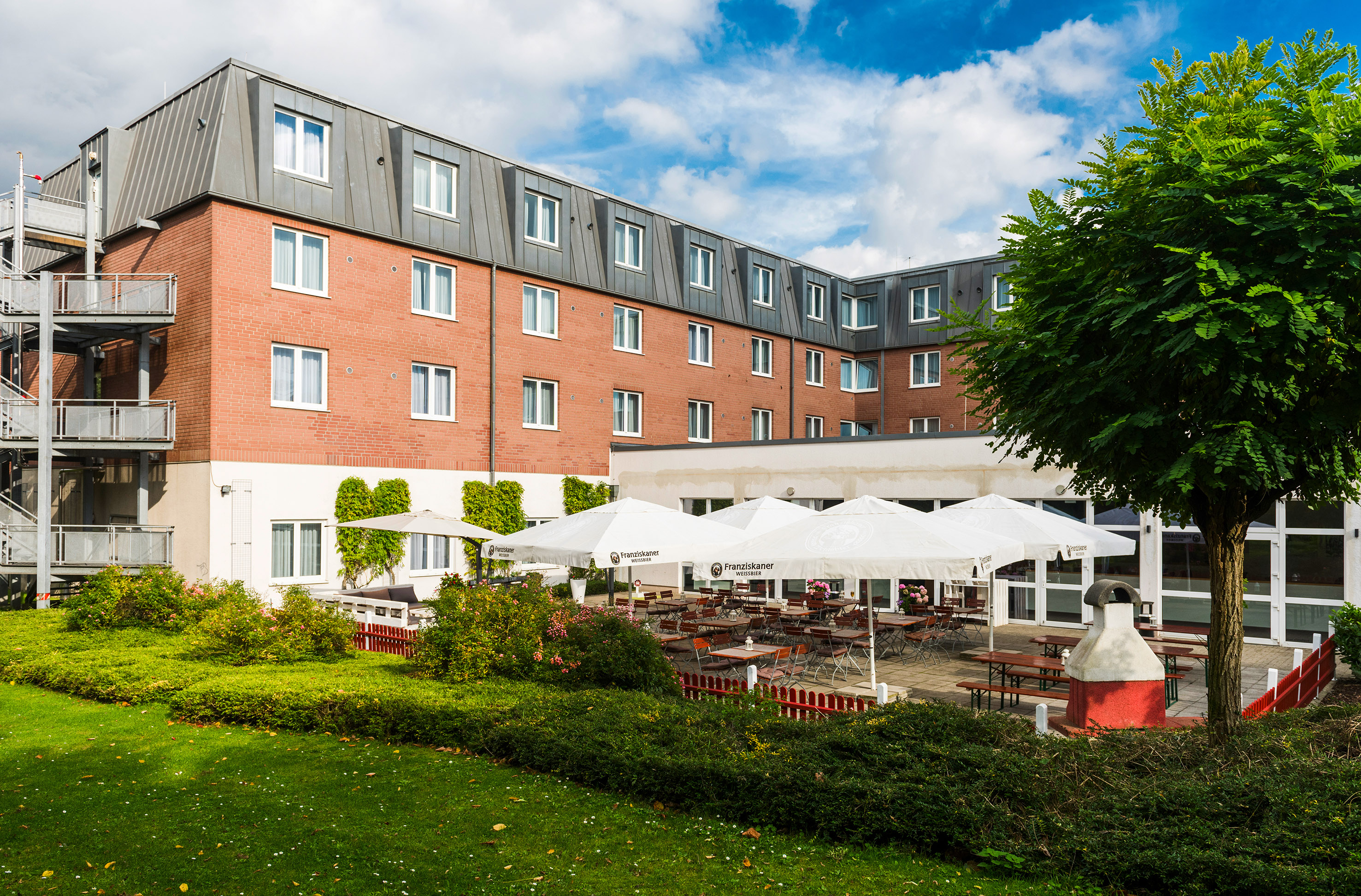 Brick hotel with outdoor dining patio, umbrellas, tables, and green lawn.