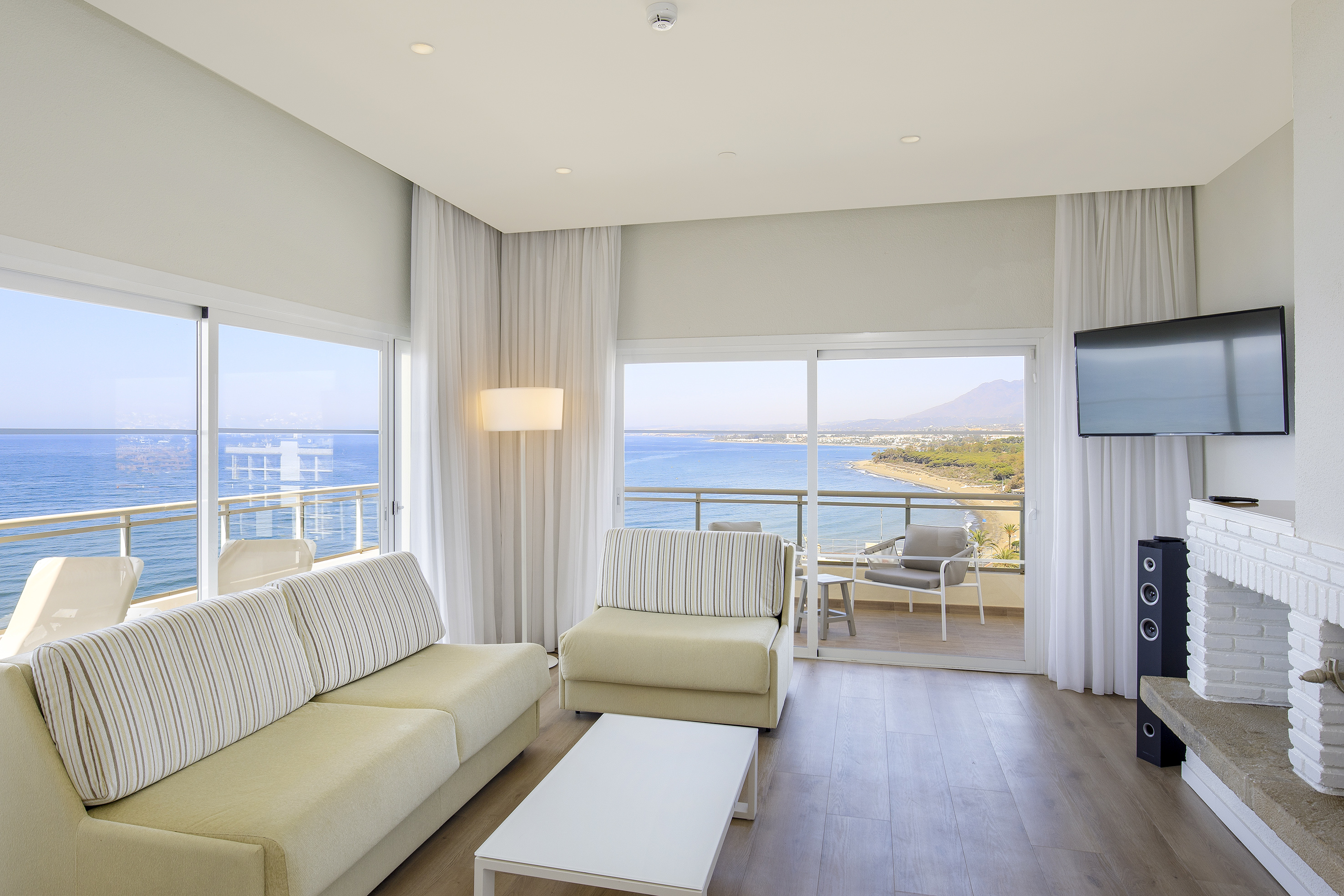 Ocean view hotel suite living room with balcony, sofa, coffee table, and TV.