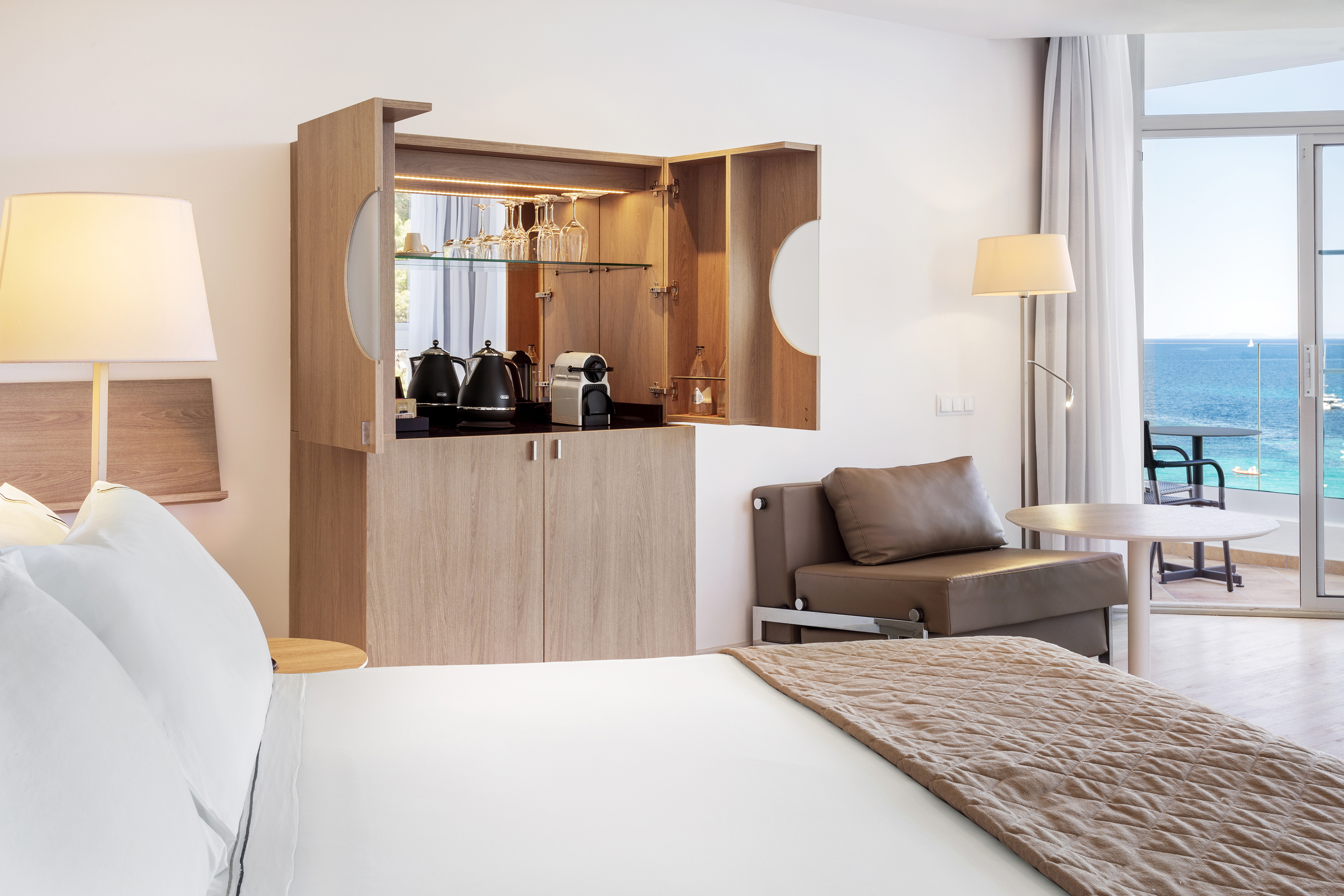 Modern hotel bedroom with ocean view, balcony, and integrated coffee station.