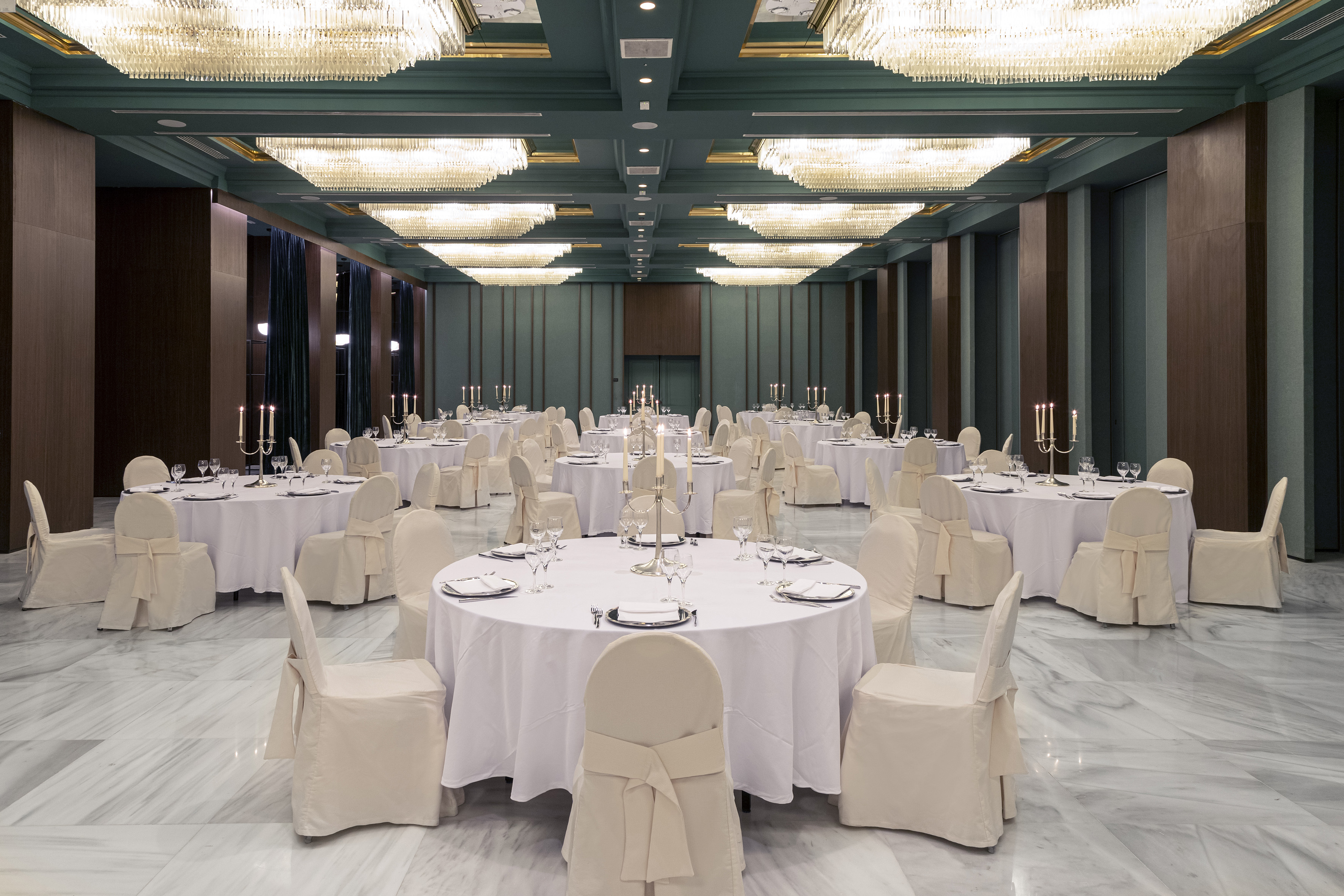 Elegant banquet hall with white tables, candelabras, and chandeliers.