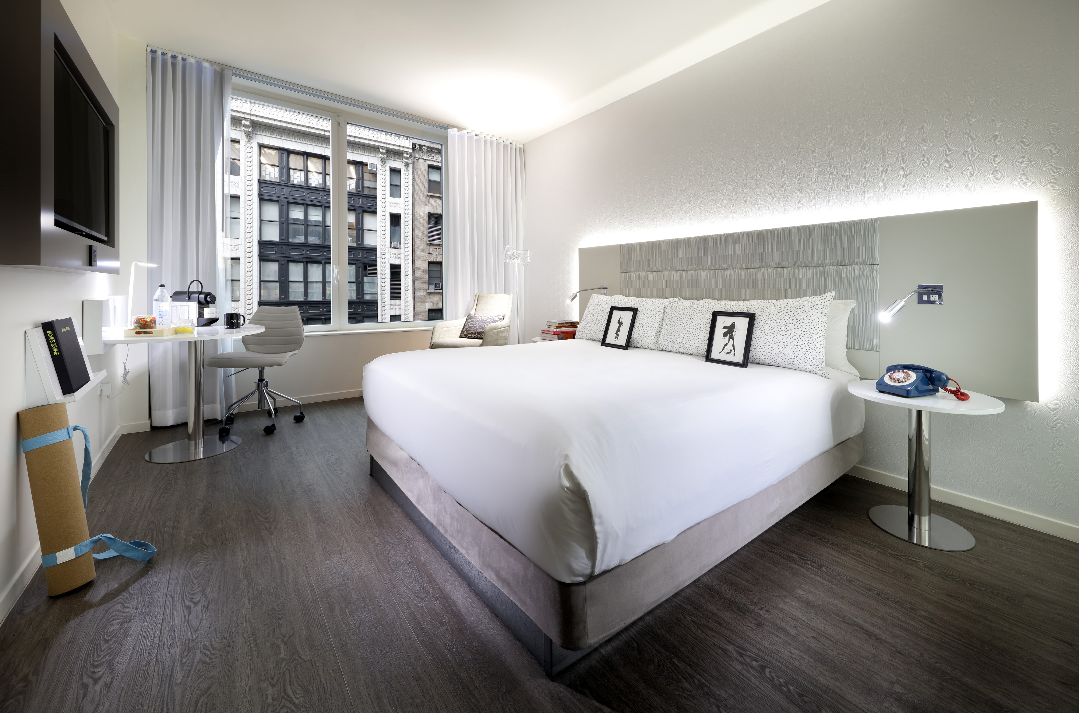 Modern hotel room with king bed, city view, desk, and yoga mat.