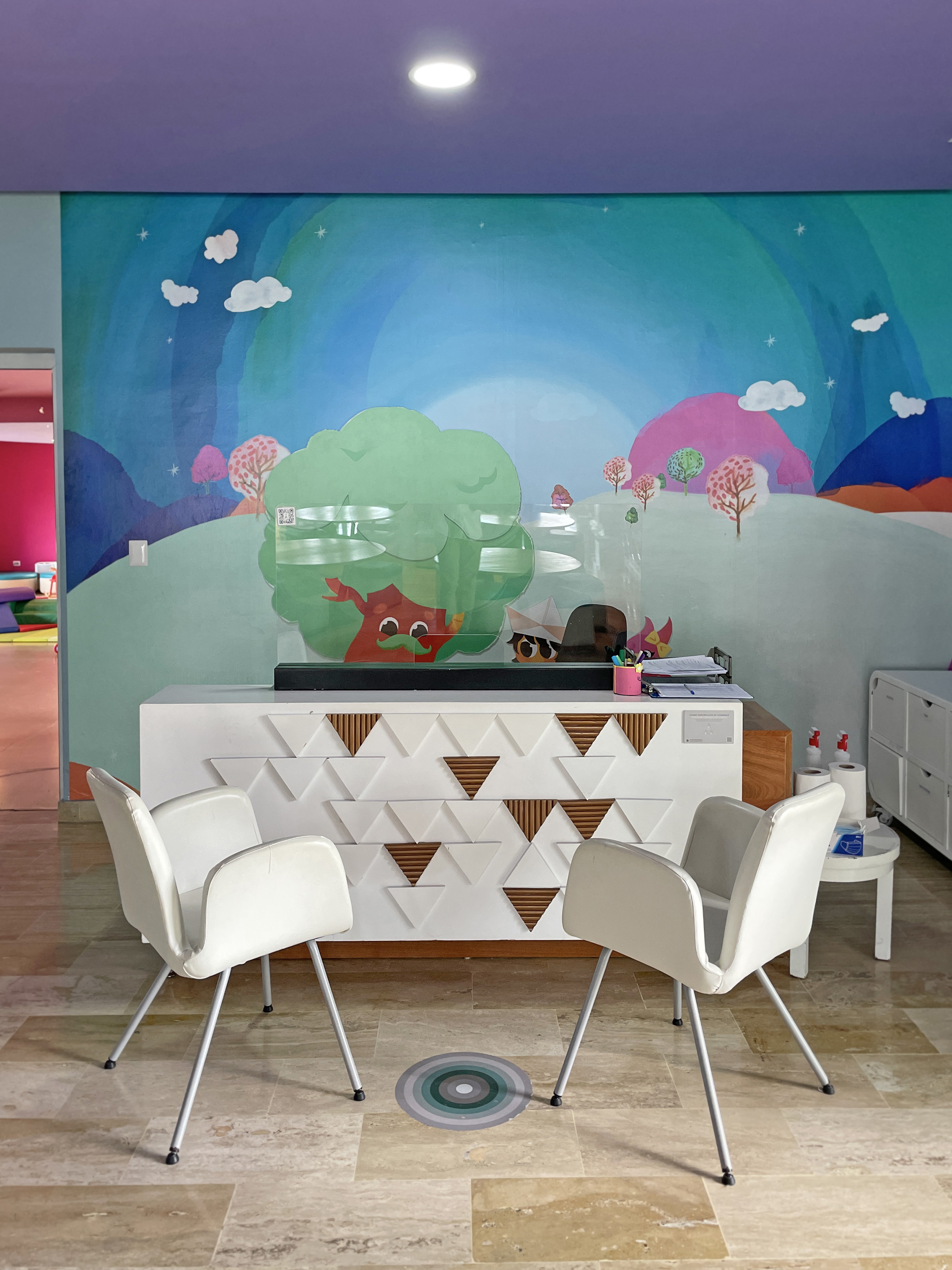 Vibrant kids' reception desk with playful mural, white chairs, and child-friendly decor.
