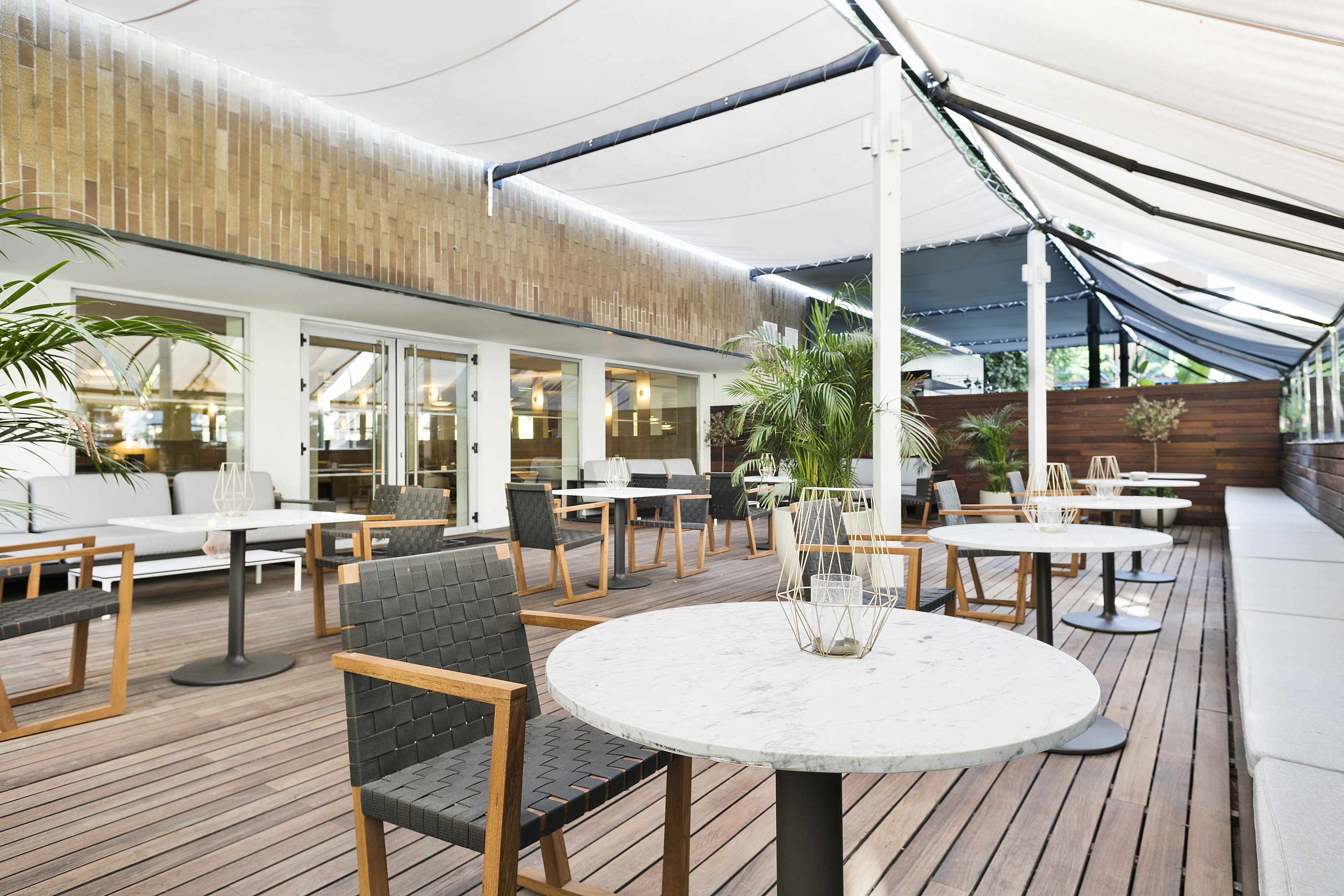 Modern outdoor dining patio with white canopy, marble tables, and wooden deck.